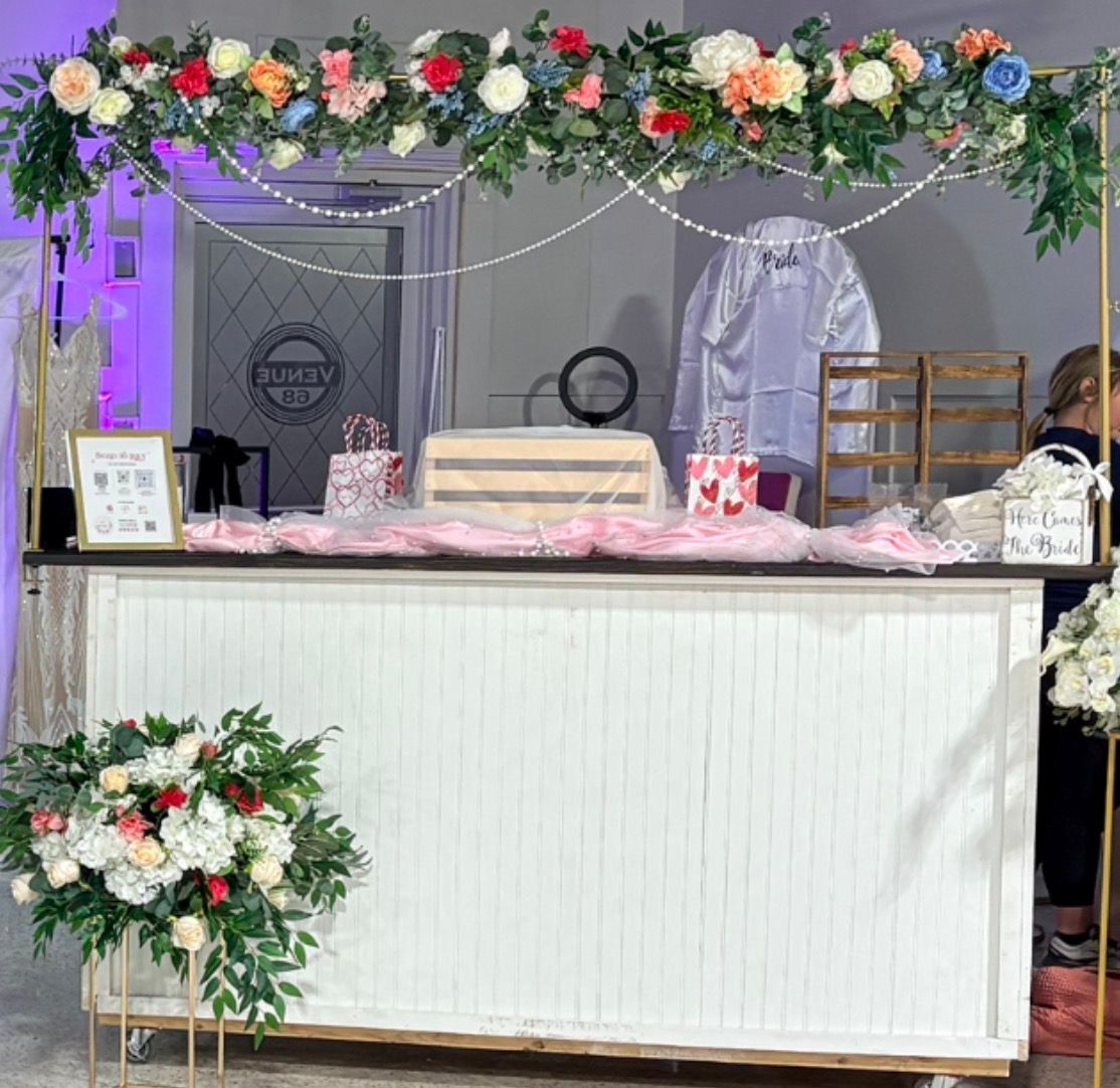 Gold tabletop floral arch decorated with colorful flowers over a wedding bar display.