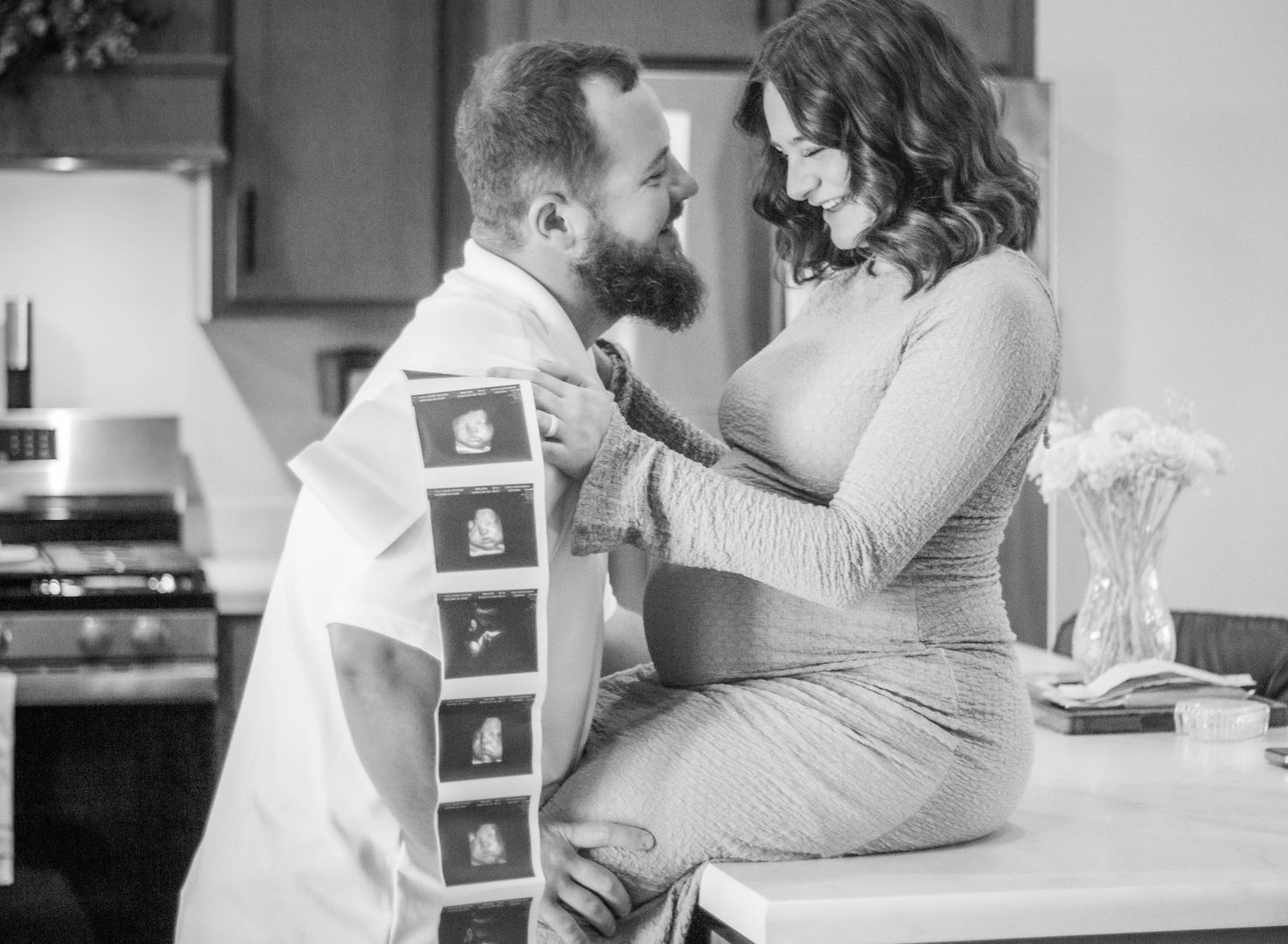 Black-and-white maternity portrait of a couple with ultrasound photos.