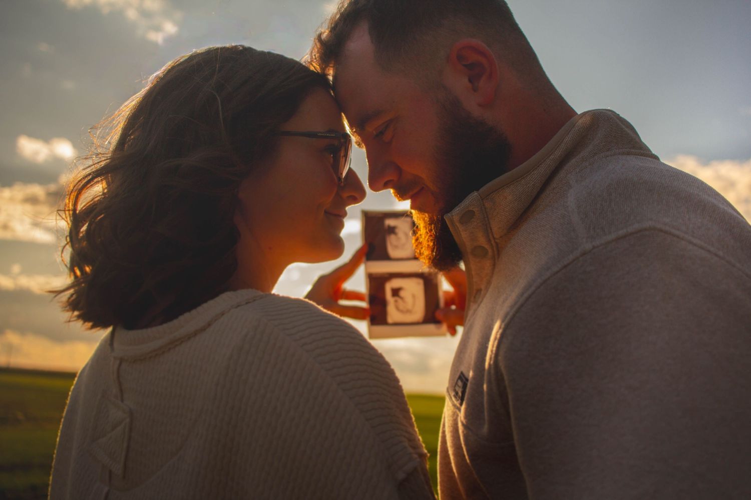 Expecting couple sharing a kiss at sunset during their pregnancy announcement session.