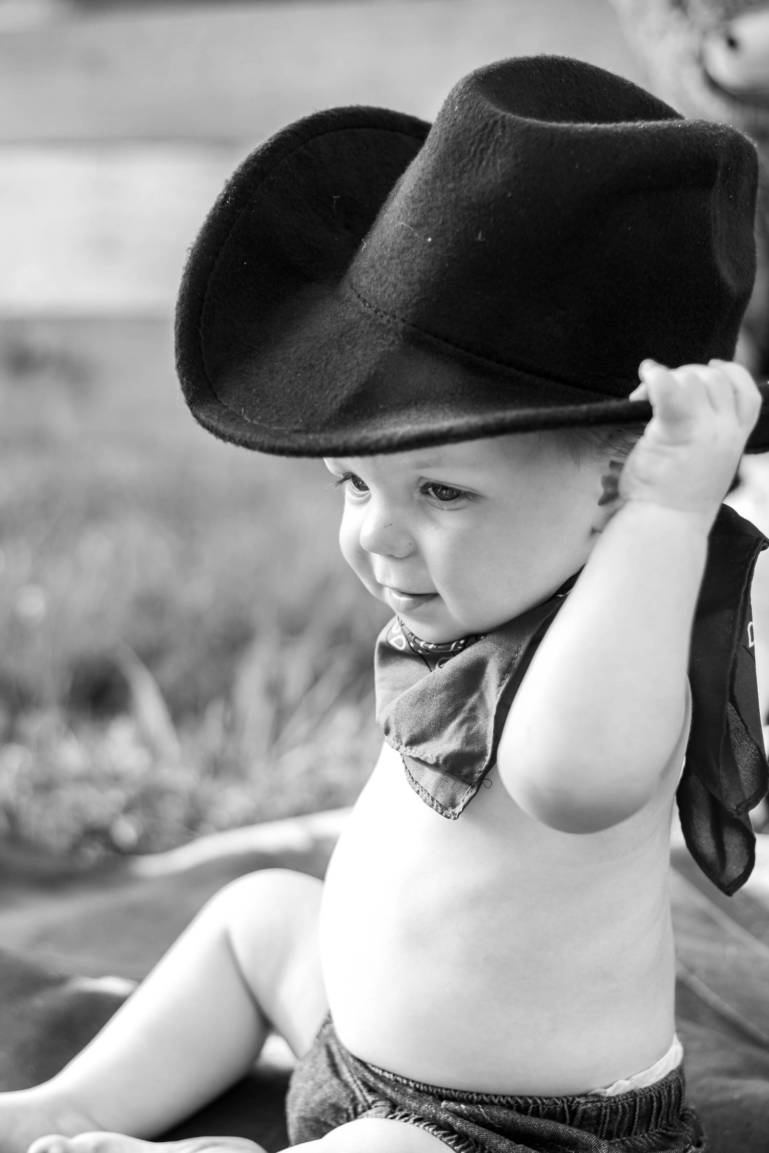 Black-and-white portrait of a baby wearing a cowboy hat outdoors.