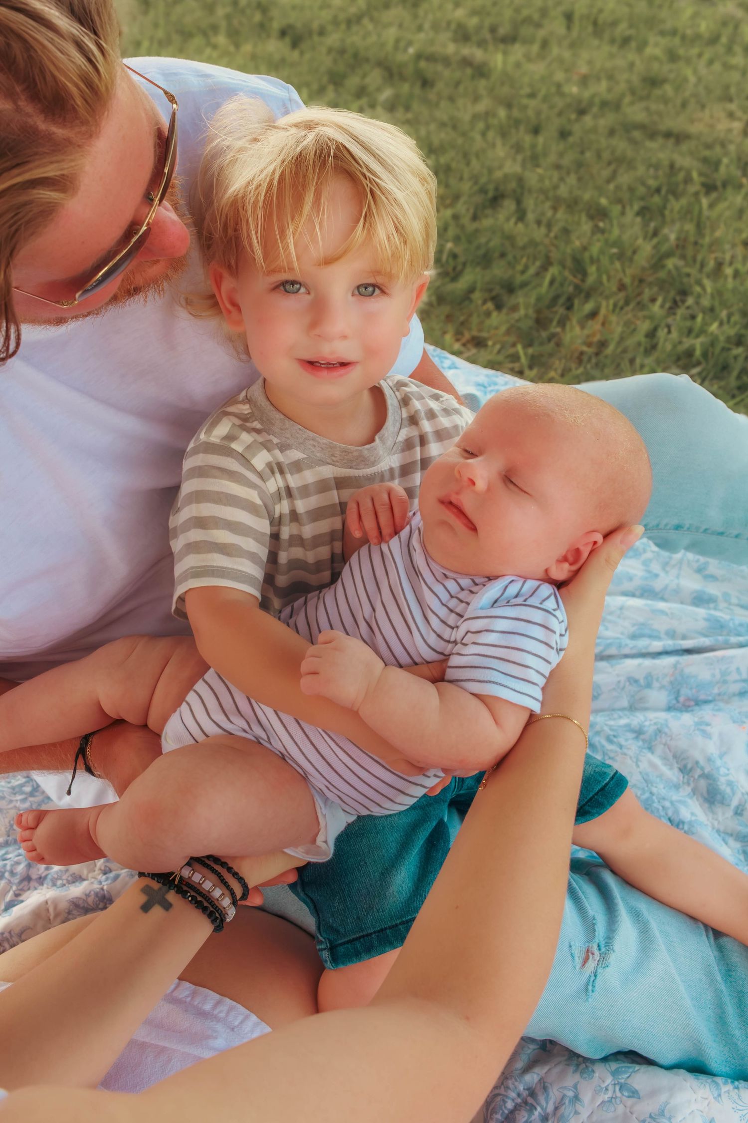 Young boy holding his baby sibling while sitting with family outdoors