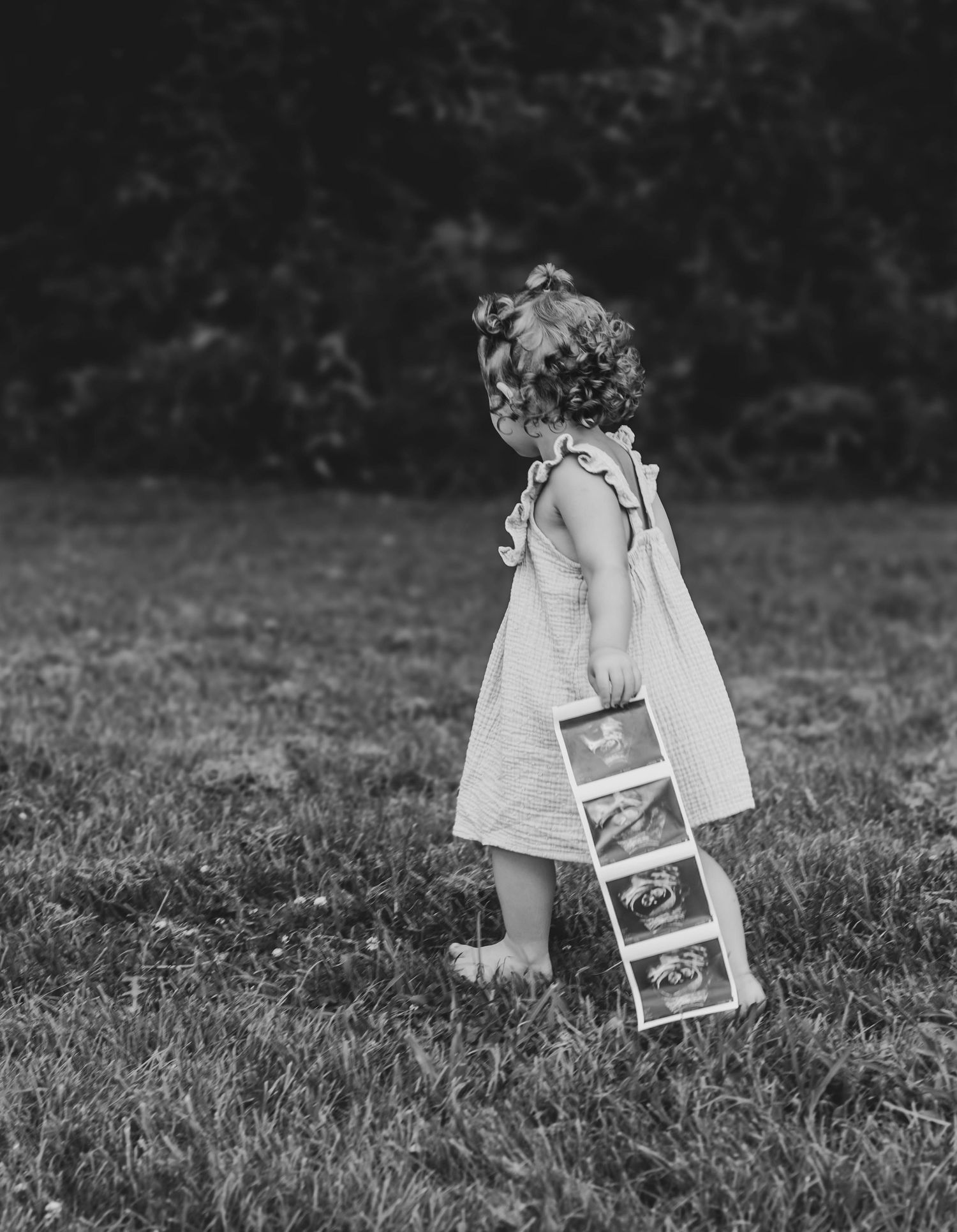 Black-and-white photo of a young girl holding ultrasound pictures in a field.