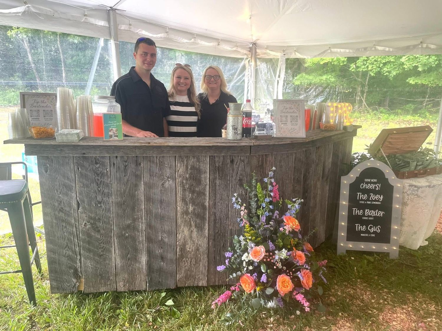 Lula's Market & More bartending team behind a rustic mobile bar at an outdoor wedding.