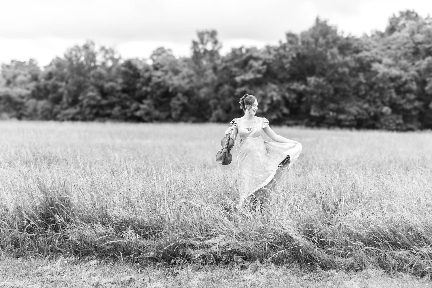 Black-and-white wide portrait of a bride walking through a field.