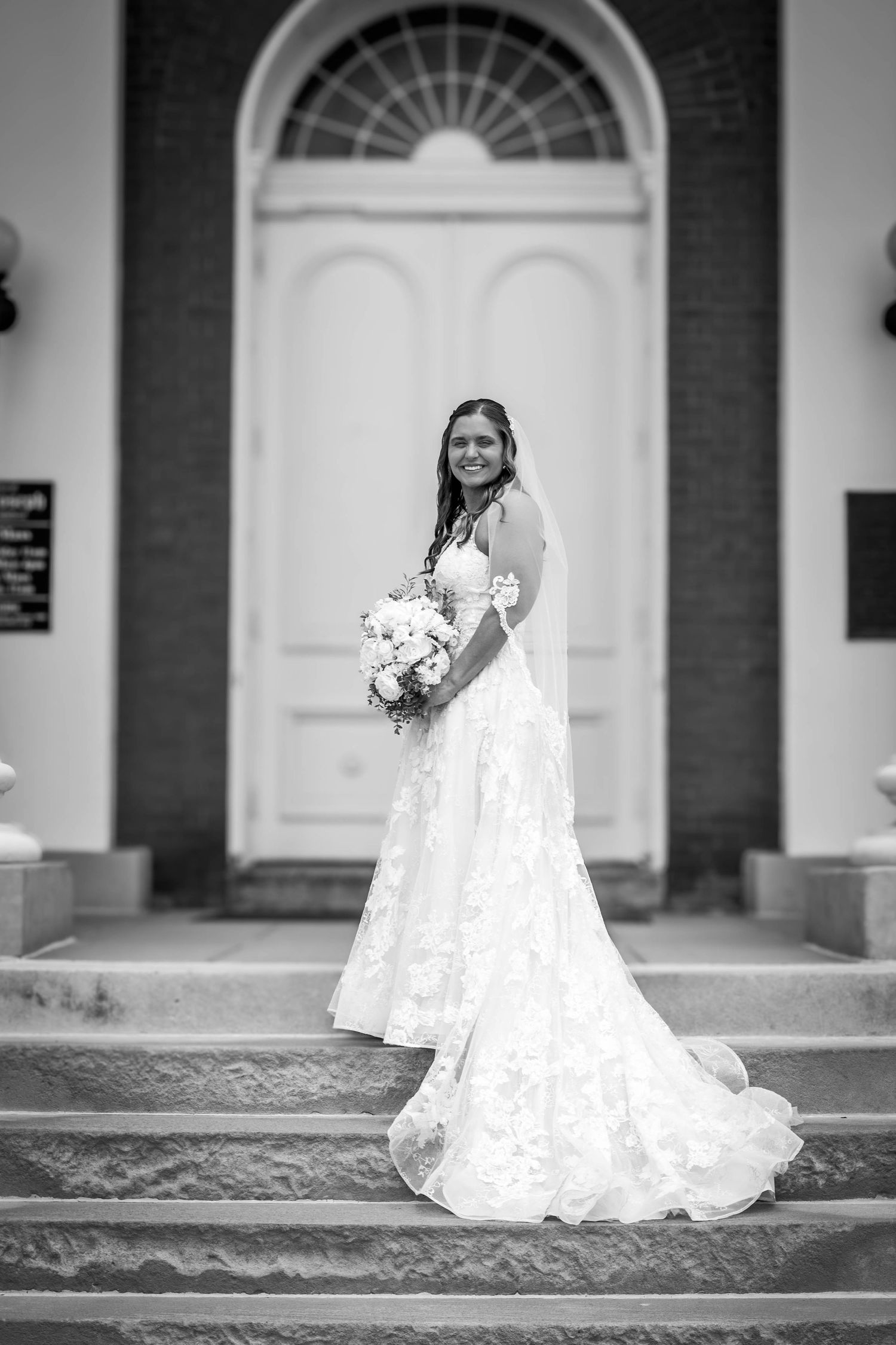 Black-and-white full-length bridal portrait outside a wedding venue