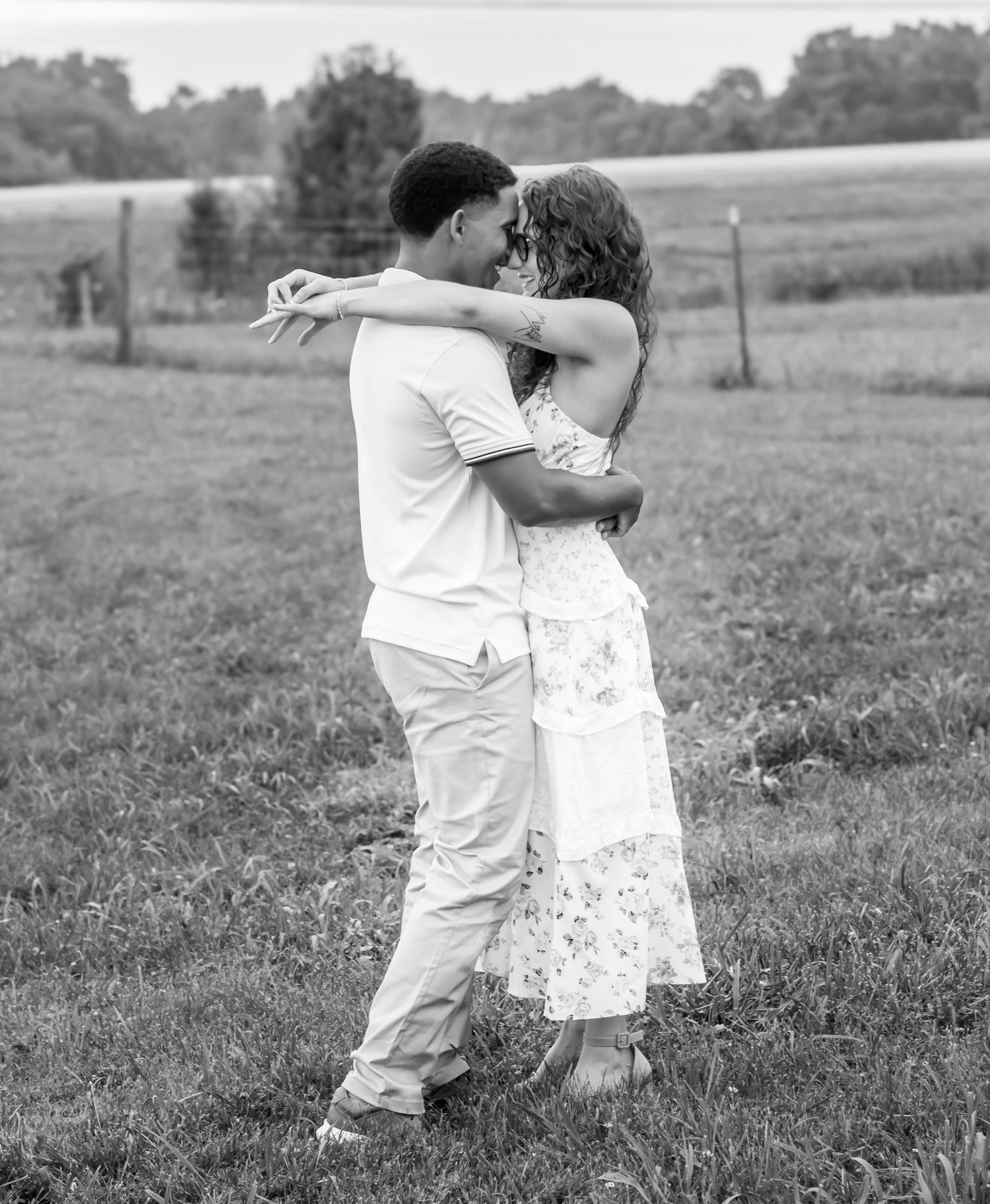Black-and-white photo of a couple embracing in an open field.