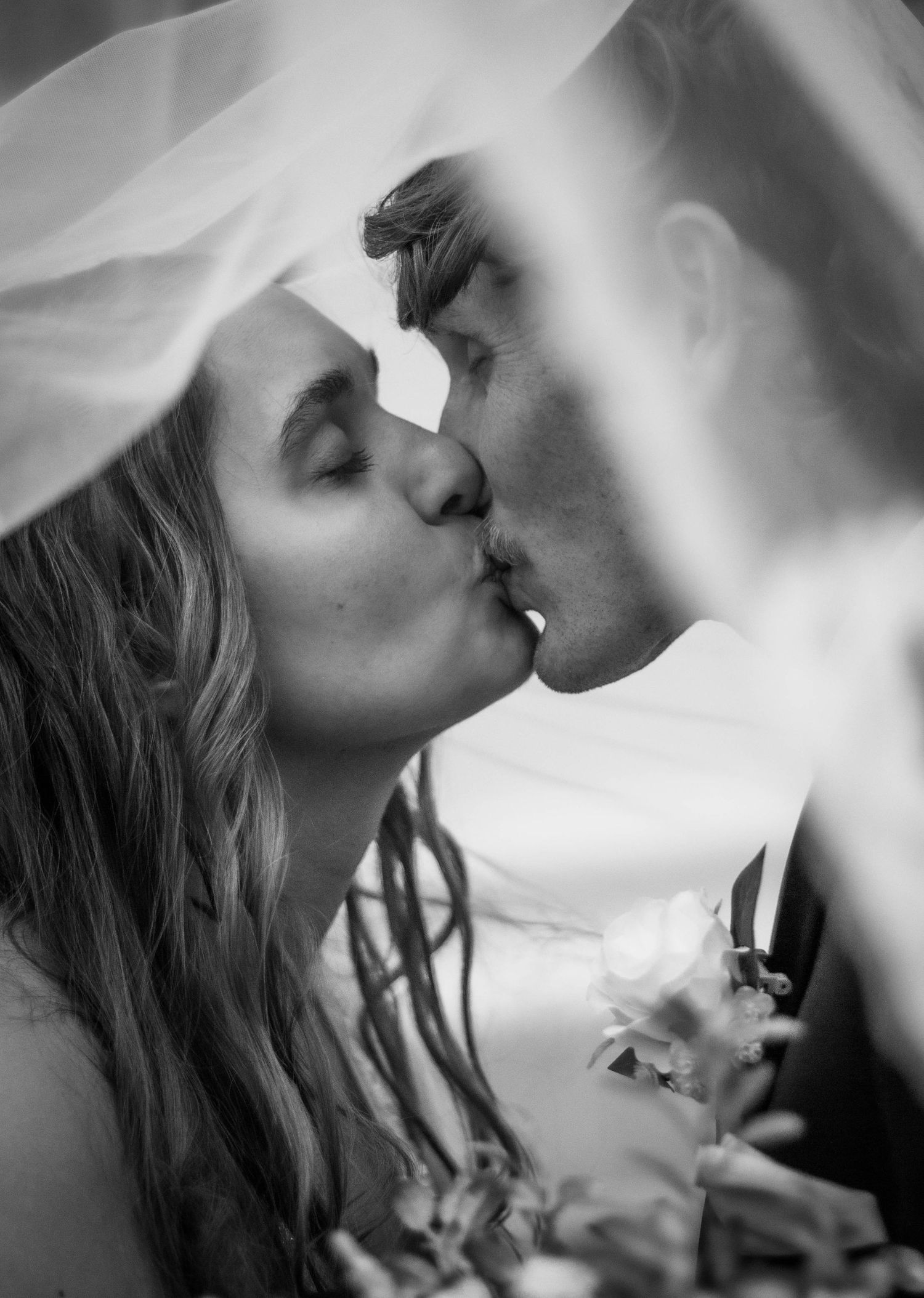Black-and-white close-up of a bride and groom kissing beneath her veil.