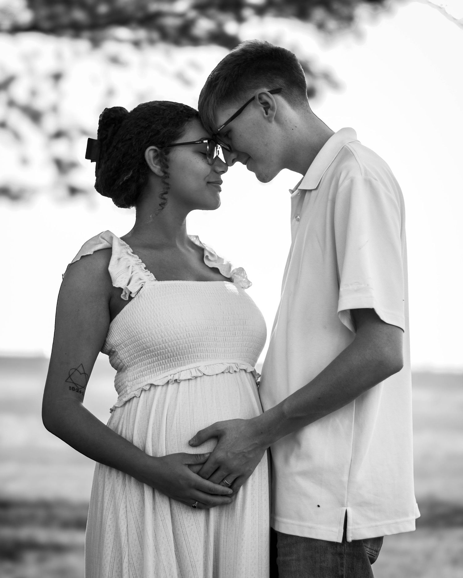 Black-and-white maternity portrait of an expecting couple standing together outdoors.
