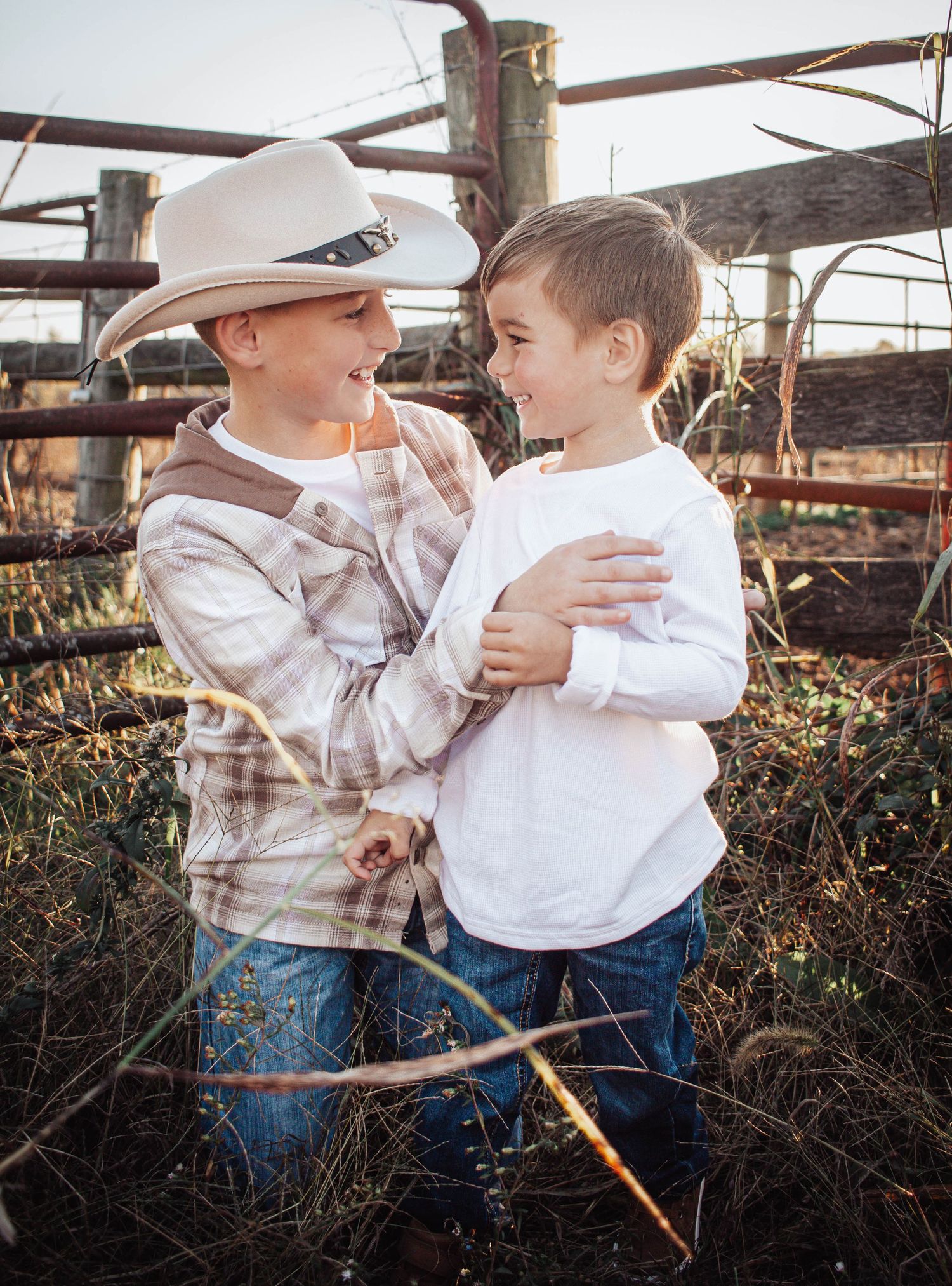 Two young brothers laughing together beside a rustic fence