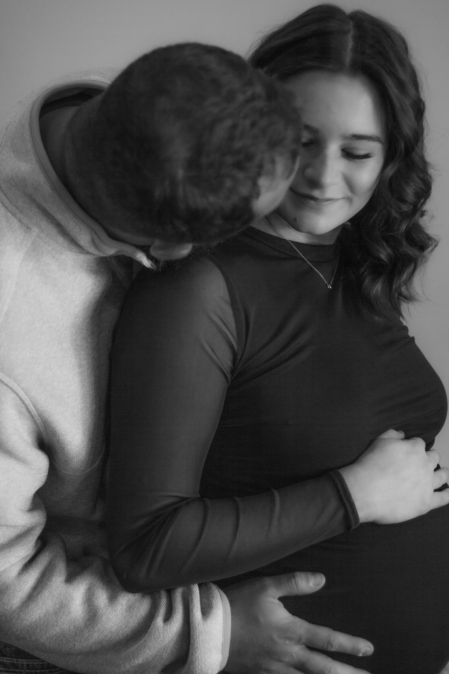 Black-and-white maternity portrait of a couple embracing and cradling the baby bump.