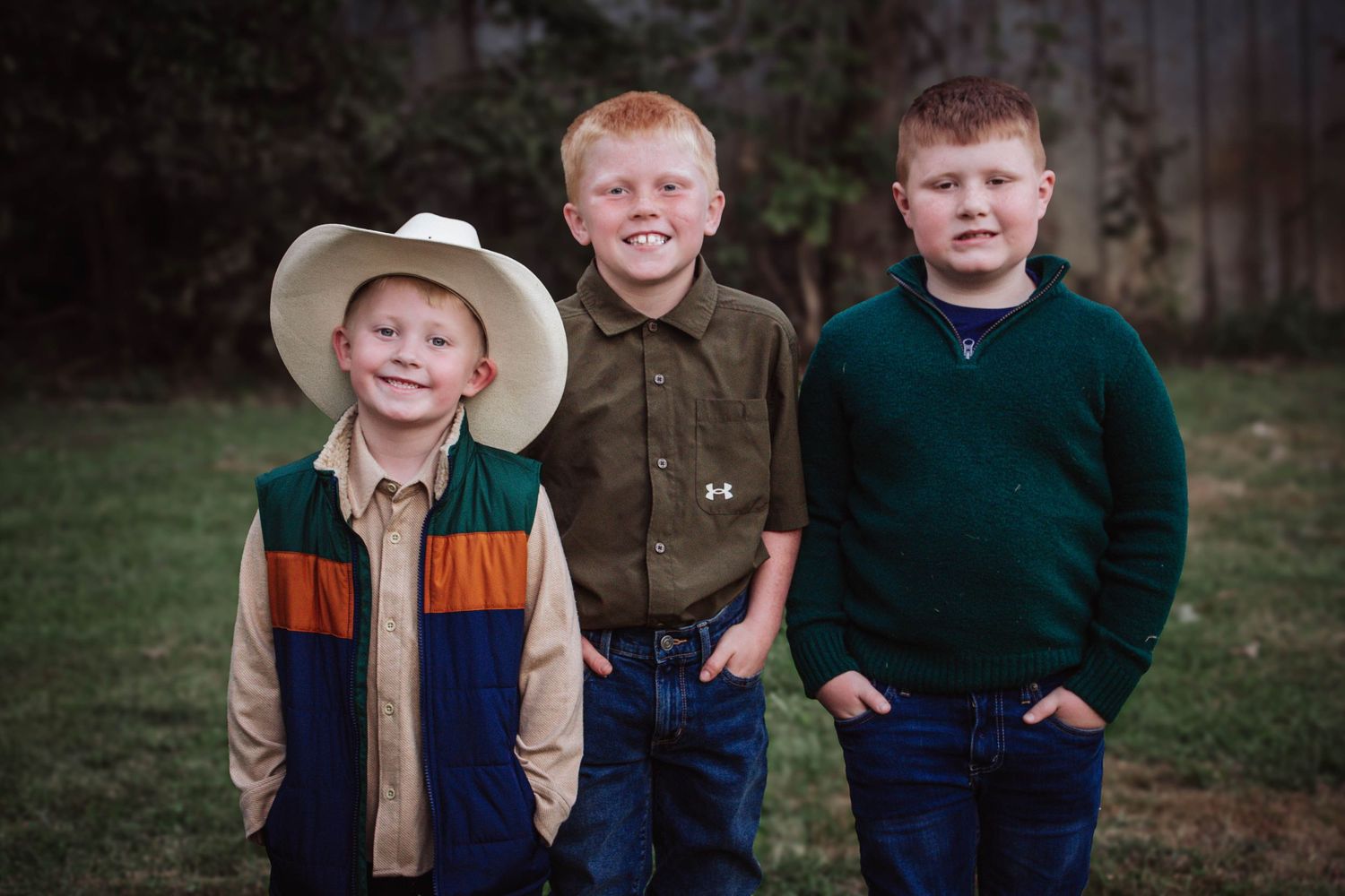 Three young boys posing together outdoors in fall clothing.