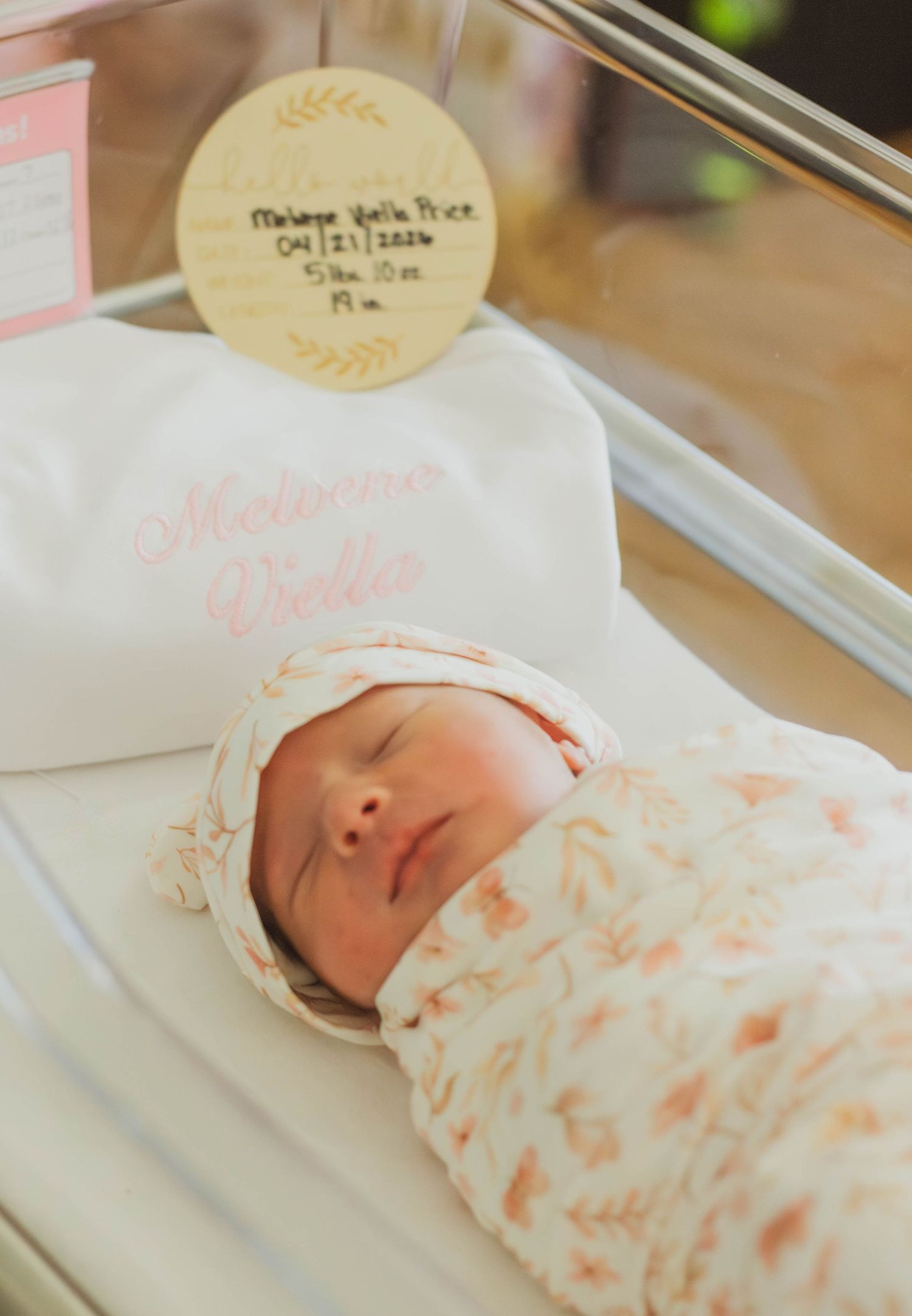 Newborn baby swaddled in a hospital bassinet with birth announcement details.