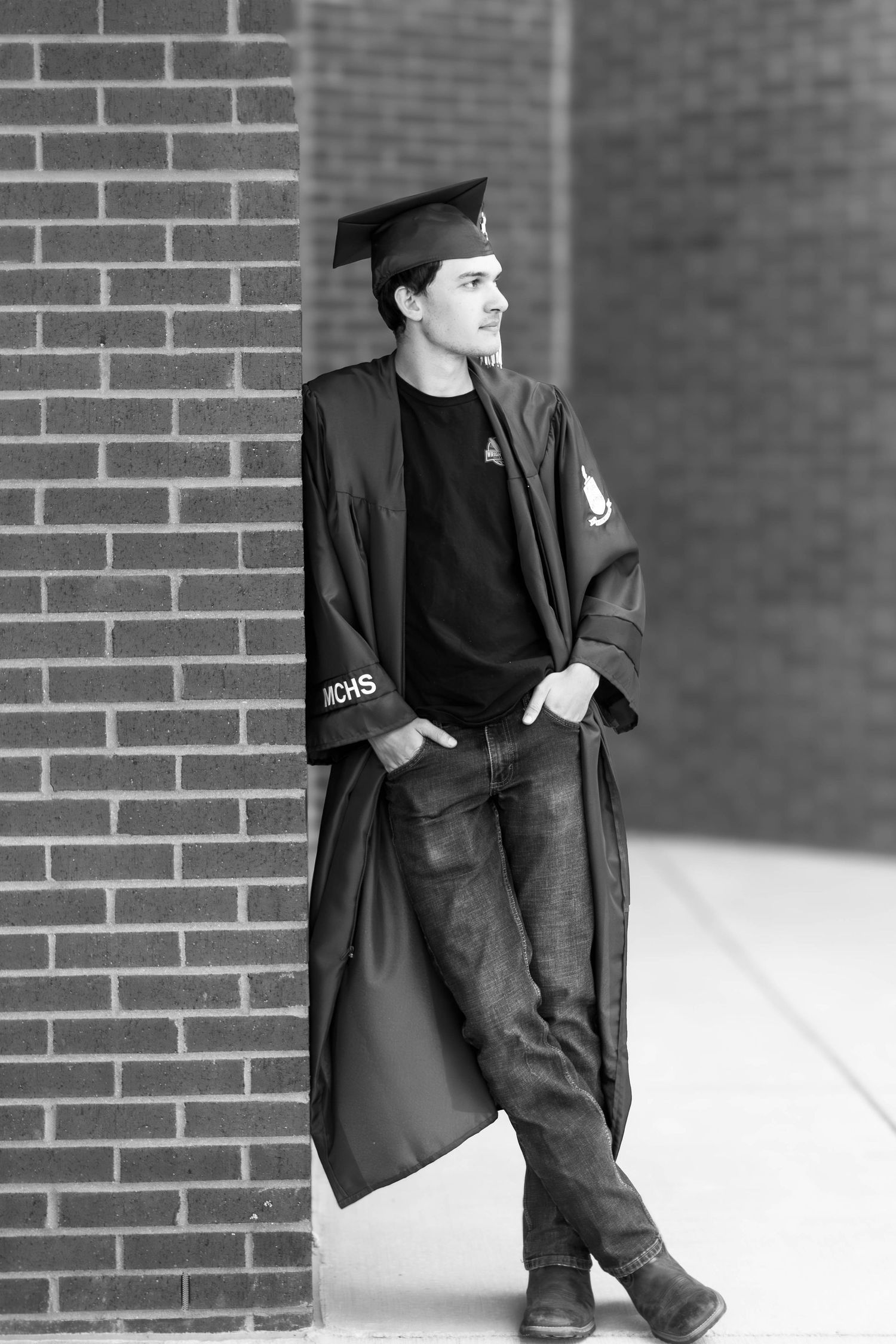 High school senior boy posing outdoors for a senior portrait session in cap and gown n black and white