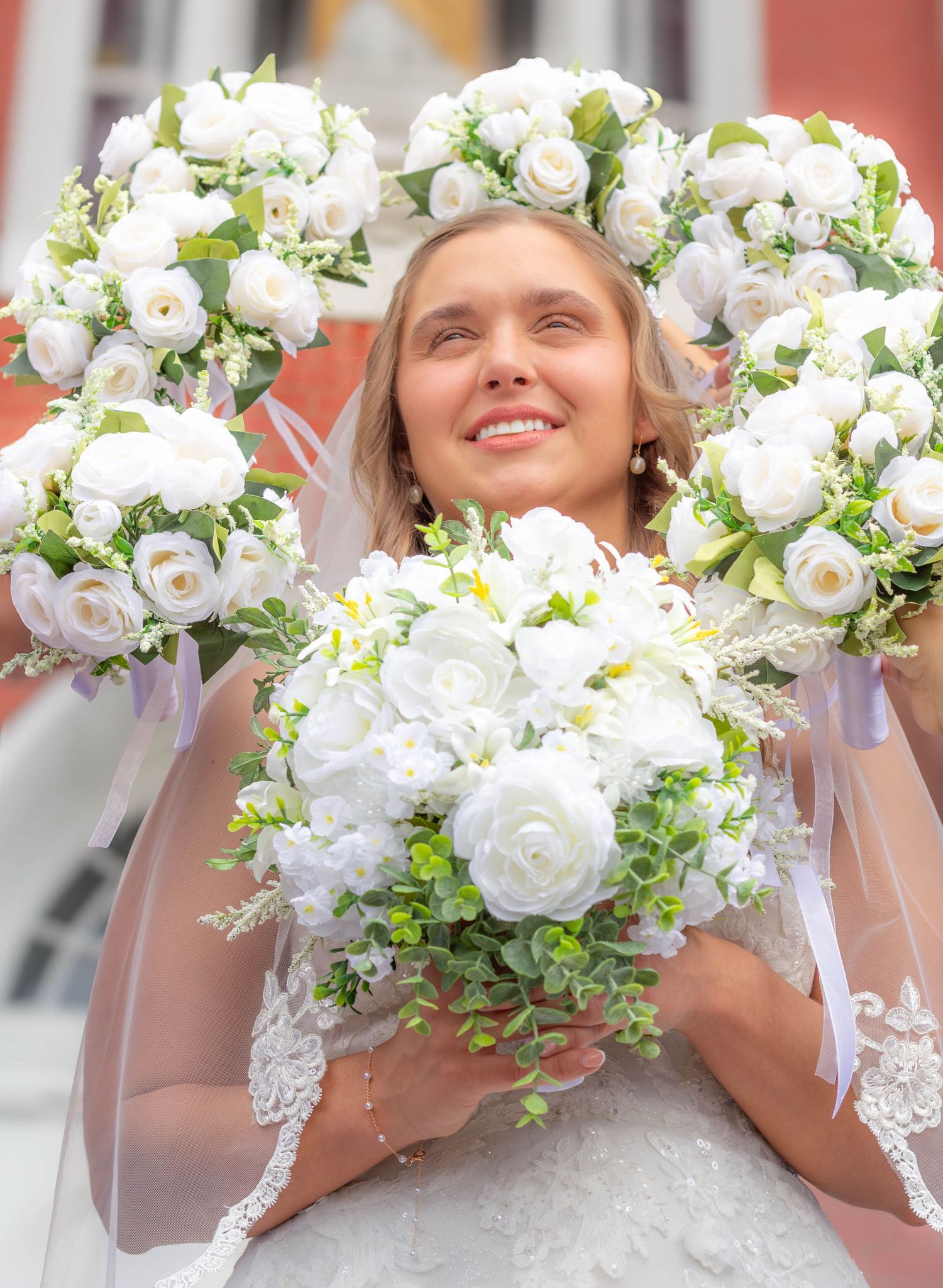 Bride smiling while holding a large white and green wedding bouquet.