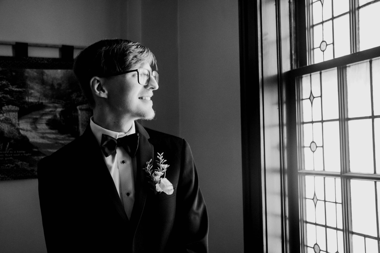 Black-and-white portrait of the groom standing beside a window.