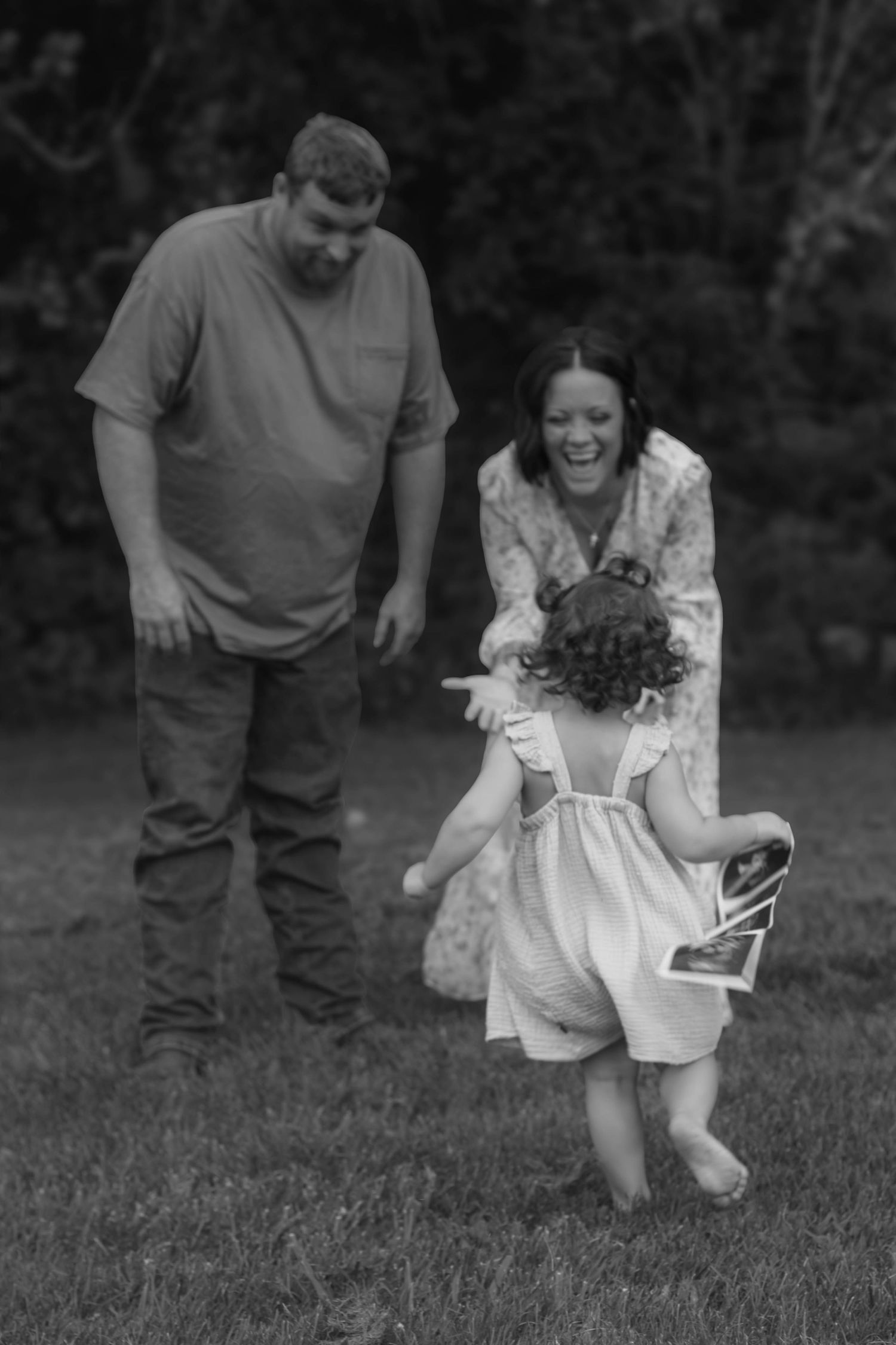 Black-and-white family maternity portrait with expectant parents and young daughter.