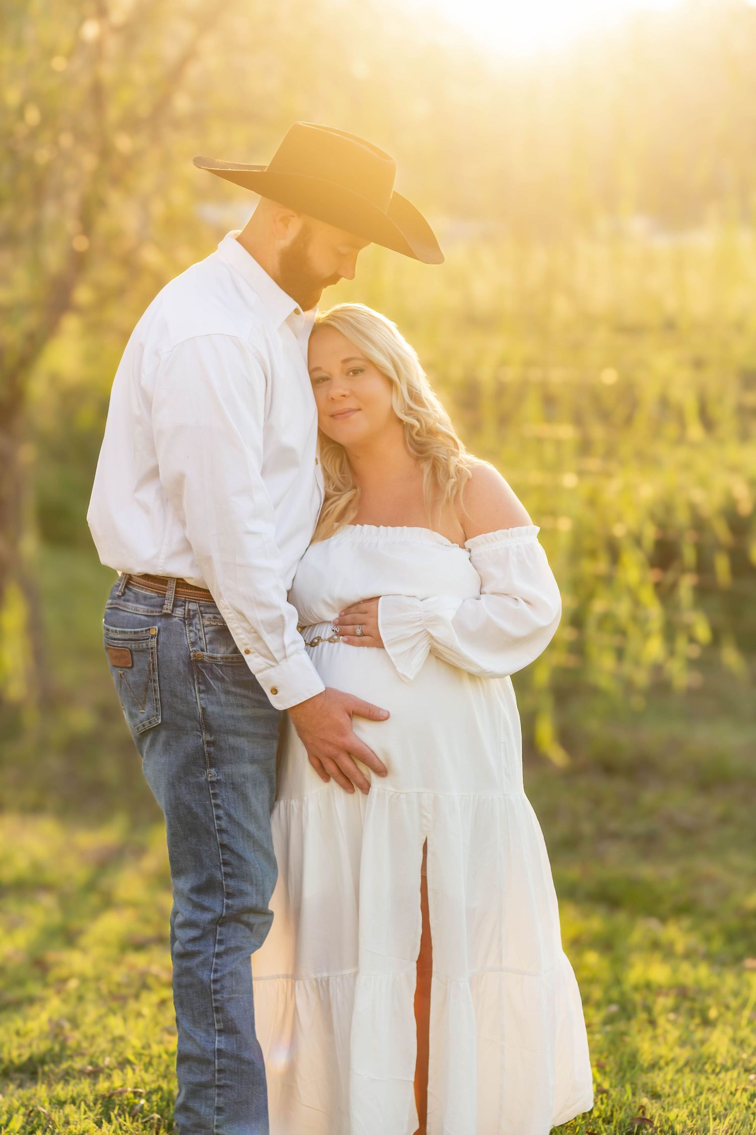 Expecting couple embracing in a field during golden-hour maternity session.