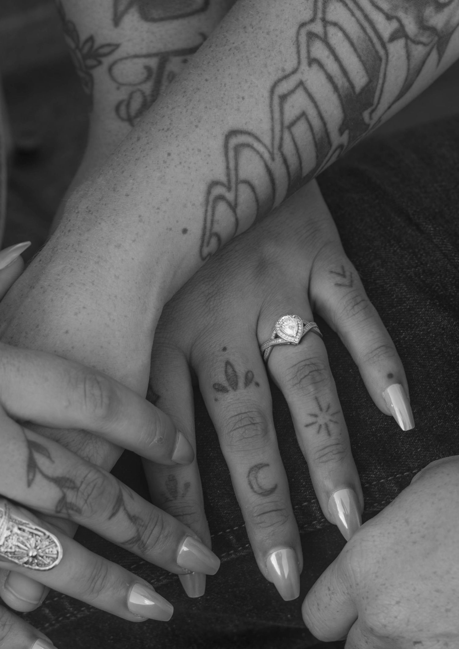 Black-and-white close-up of an engagement ring on intertwined hands.