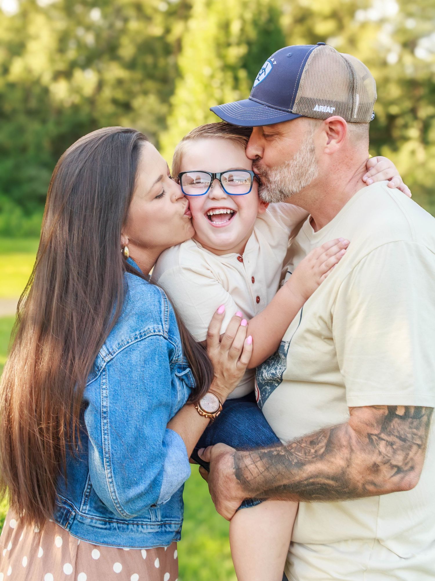 Parents kissing their smiling young son during an outdoor family photography session.”