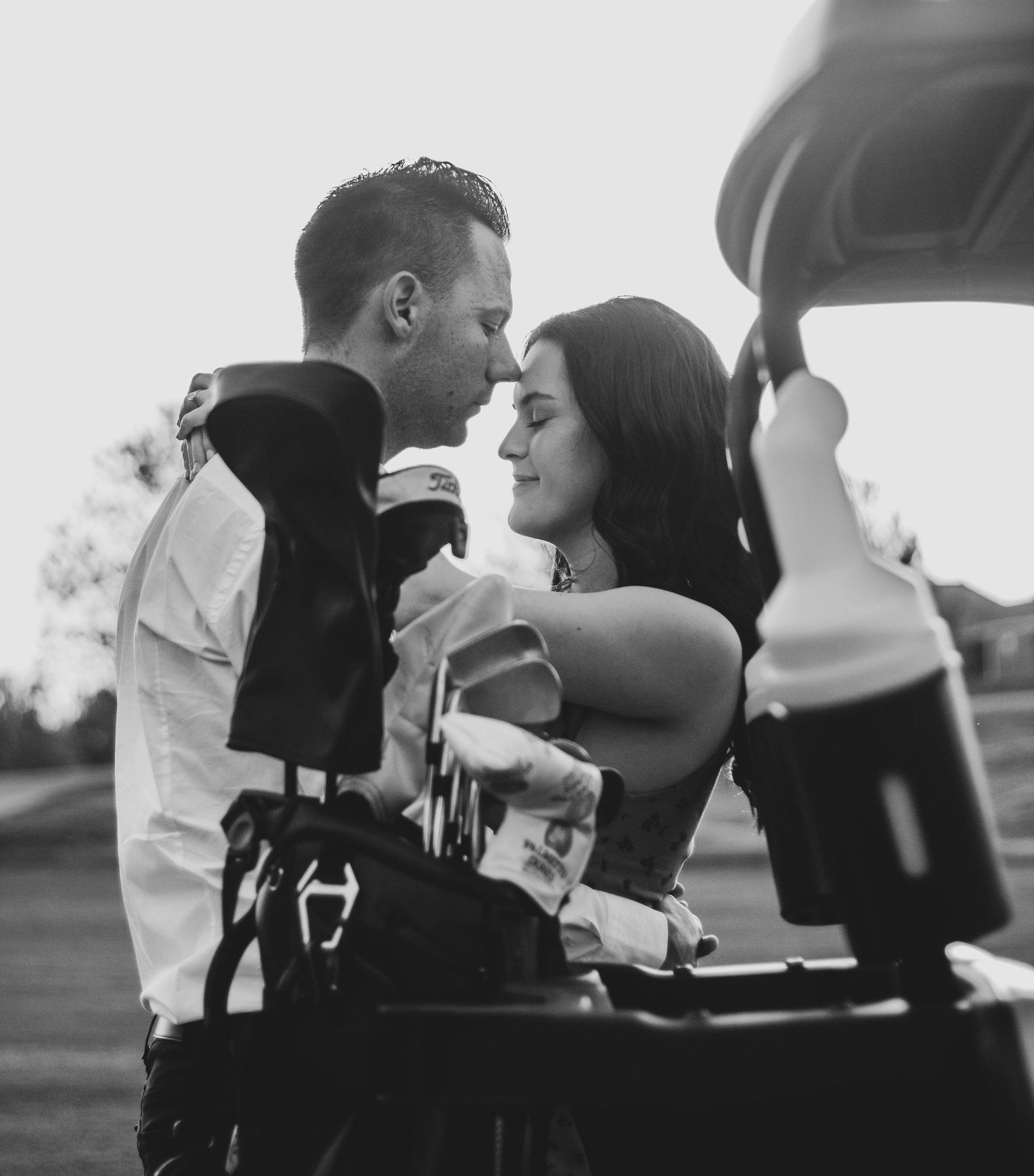 Black-and-white candid of a couple together beside a golf cart.