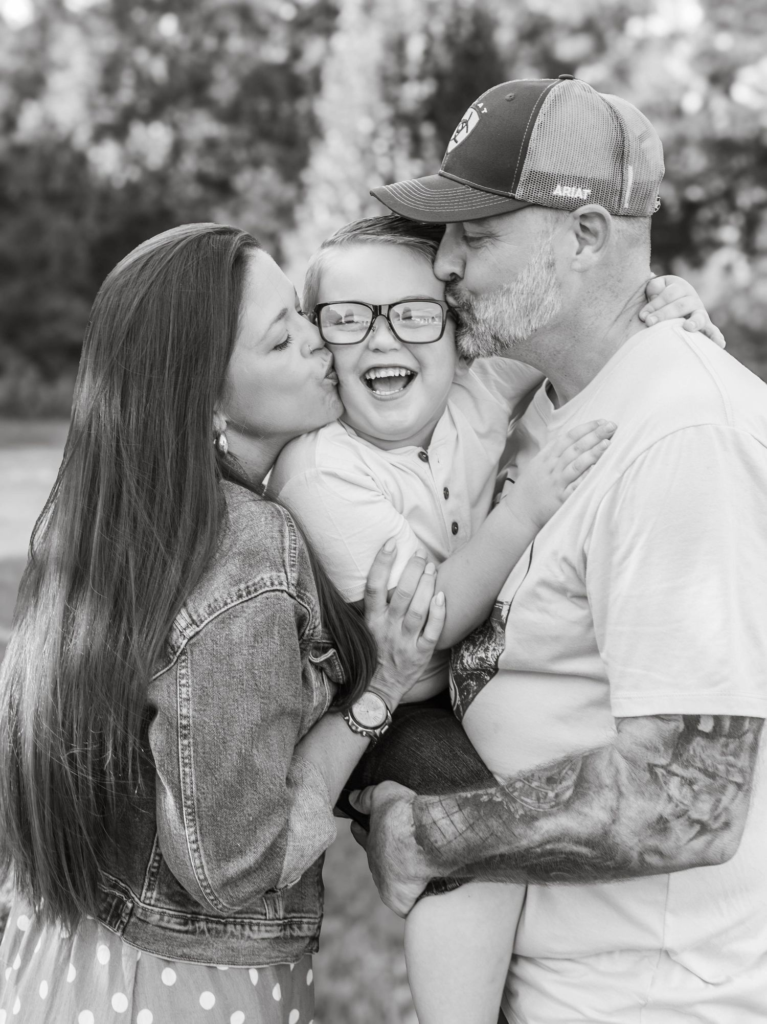 Parents kissing their smiling son during a candid black-and-white family portrait
