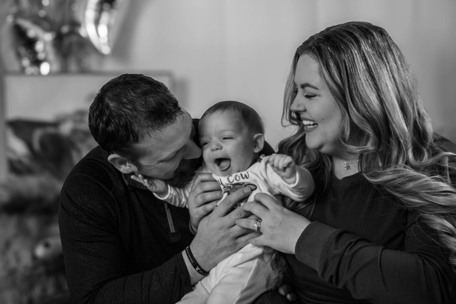 Black-and-white family portrait of parents holding their baby.