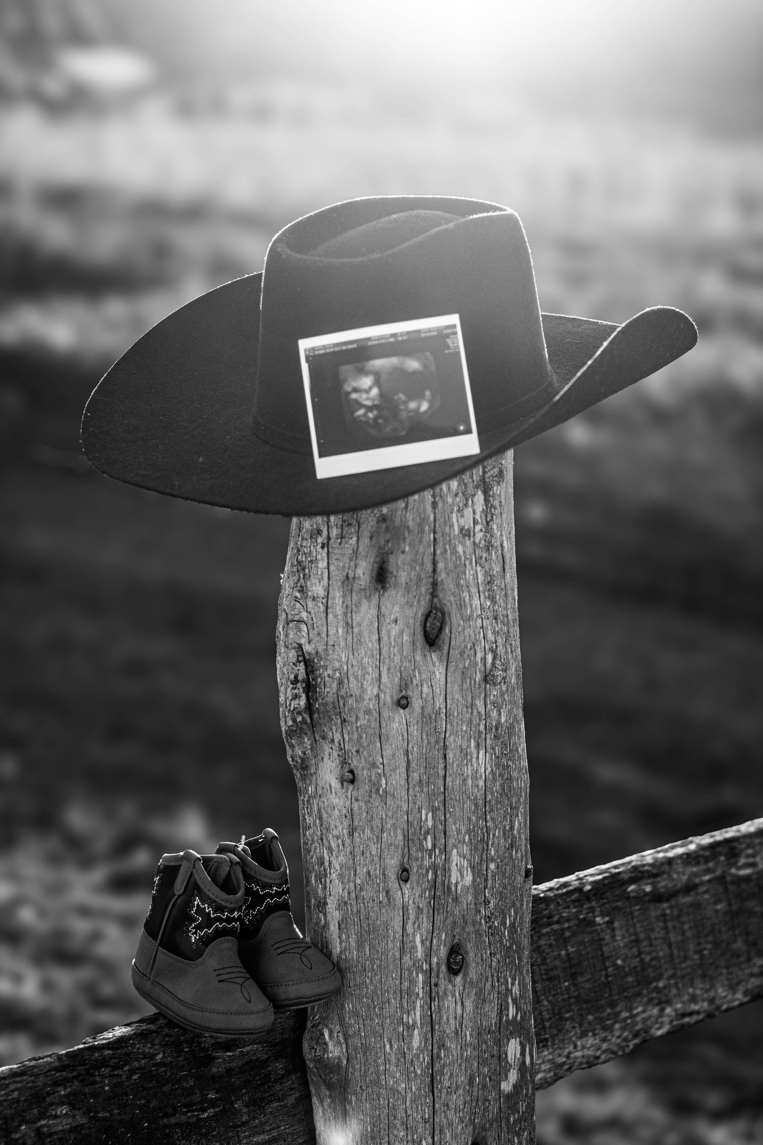 Black-and-white pregnancy announcement with cowboy hat, baby shoes, and ultrasound photo.