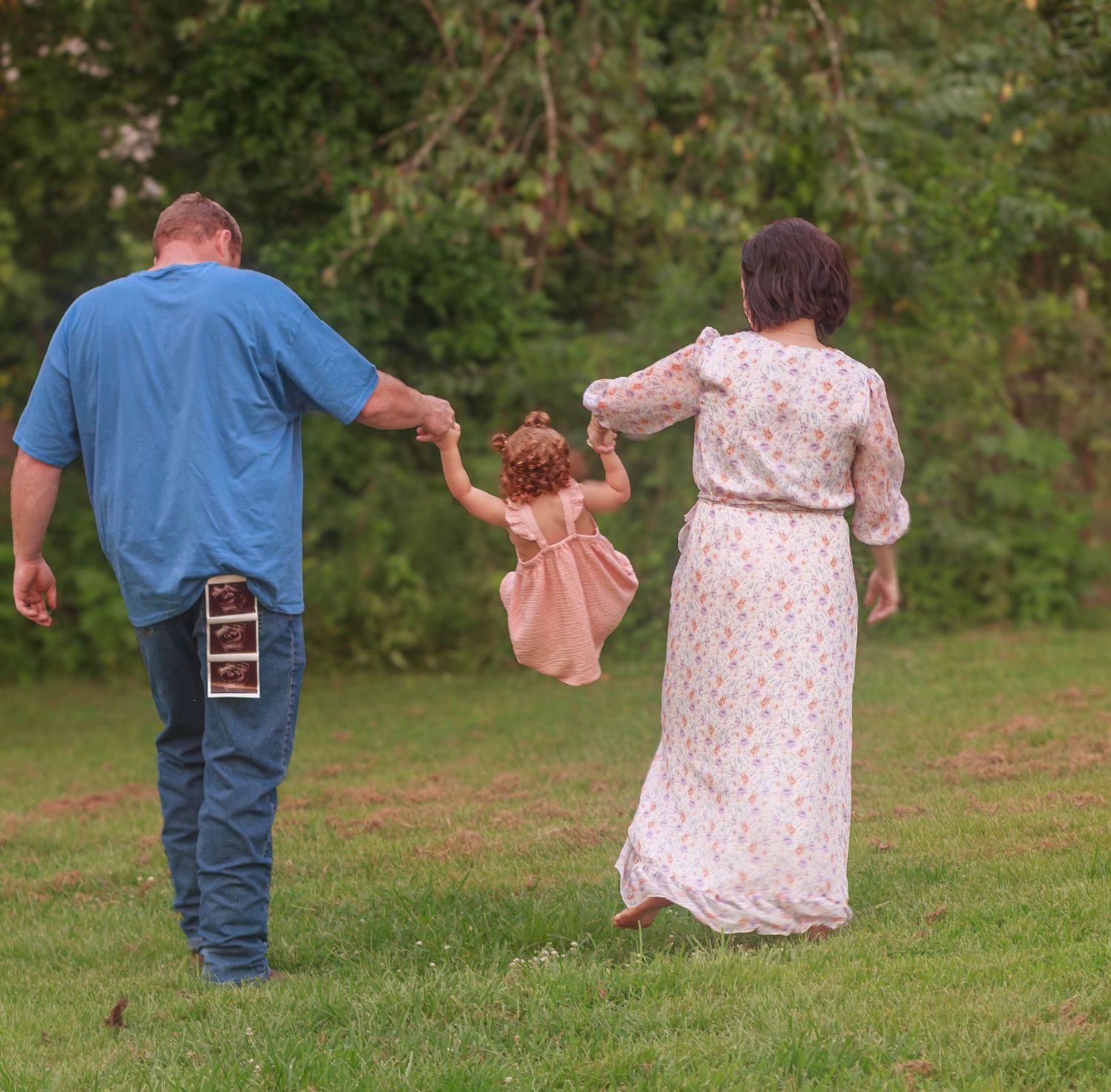 Expecting parents walking hand in hand with their young daughter outdoors.