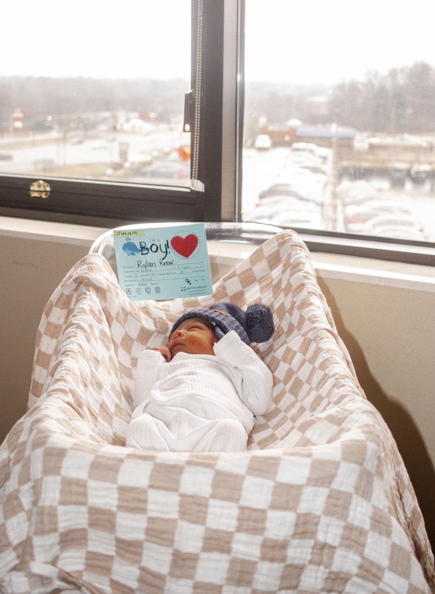 Newborn baby resting in a hospital bassinet near a window.