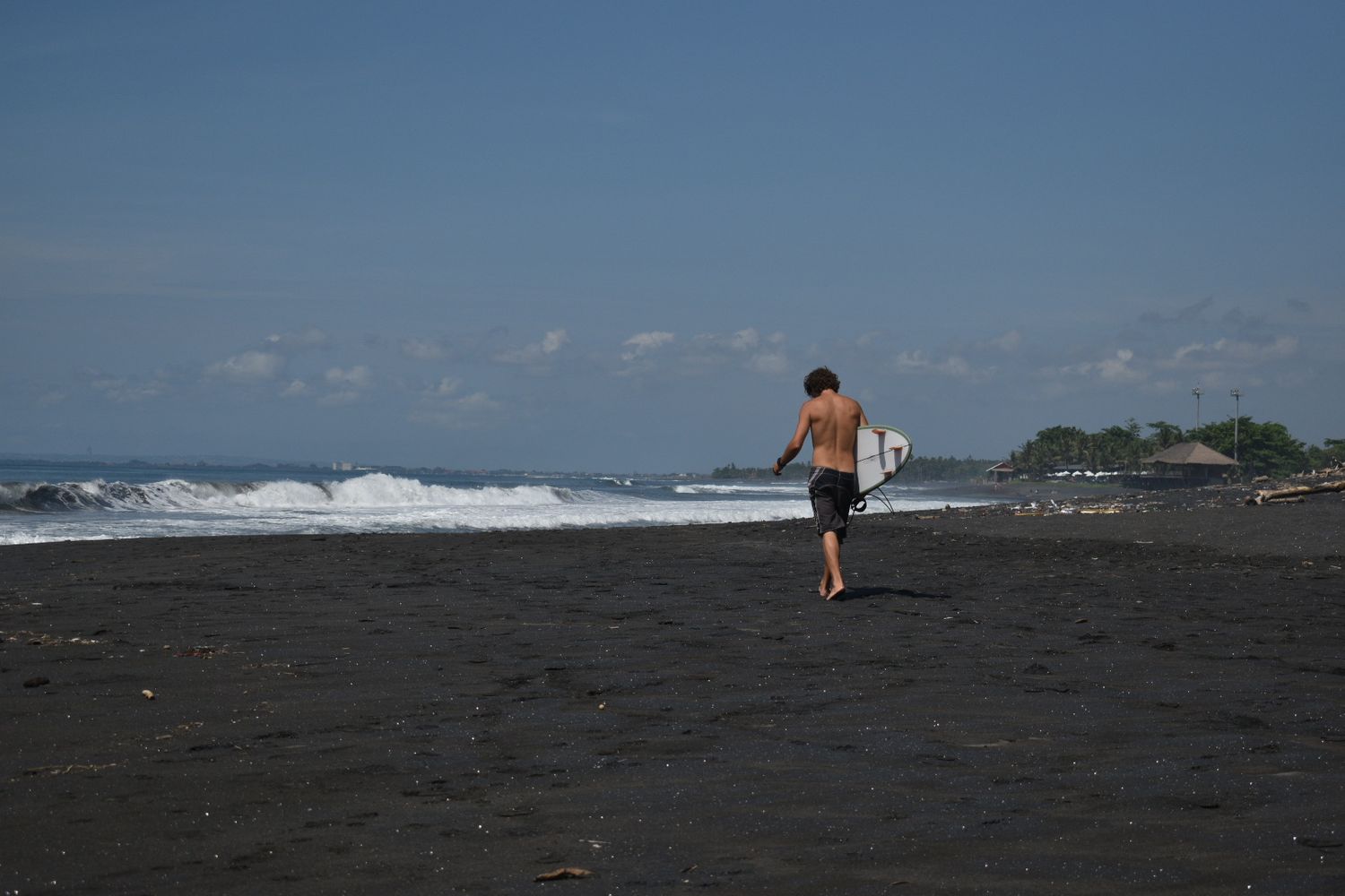 Candid photograph of a surfer on a black sand beach in Bali.