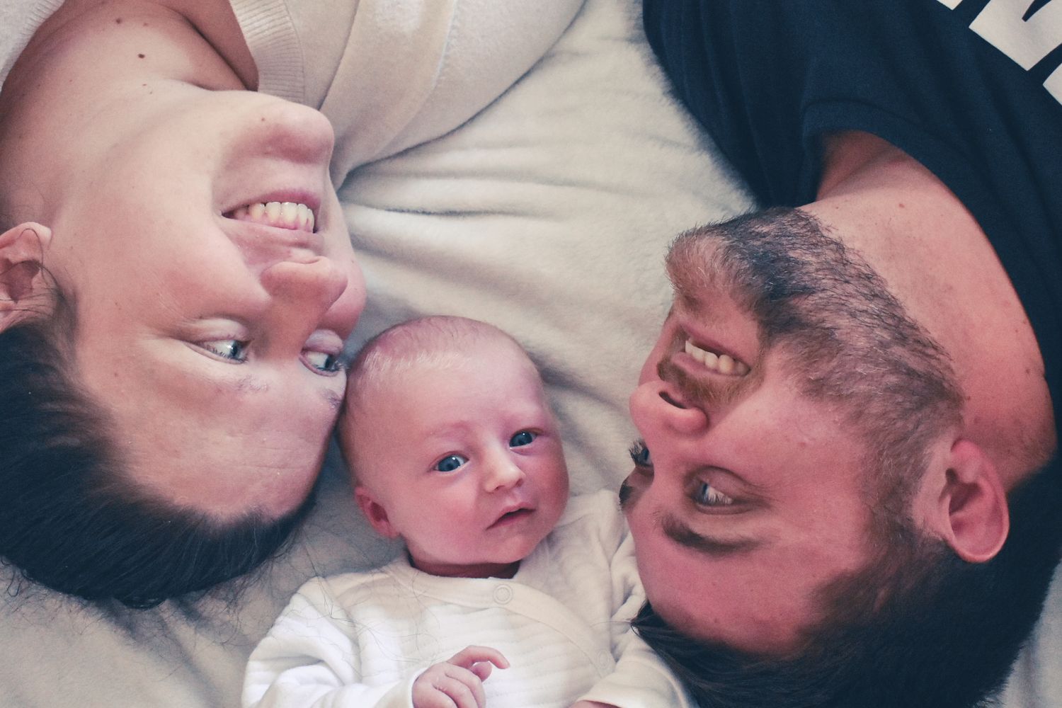 Mom and dad laughing at their baby in a new born shoot.