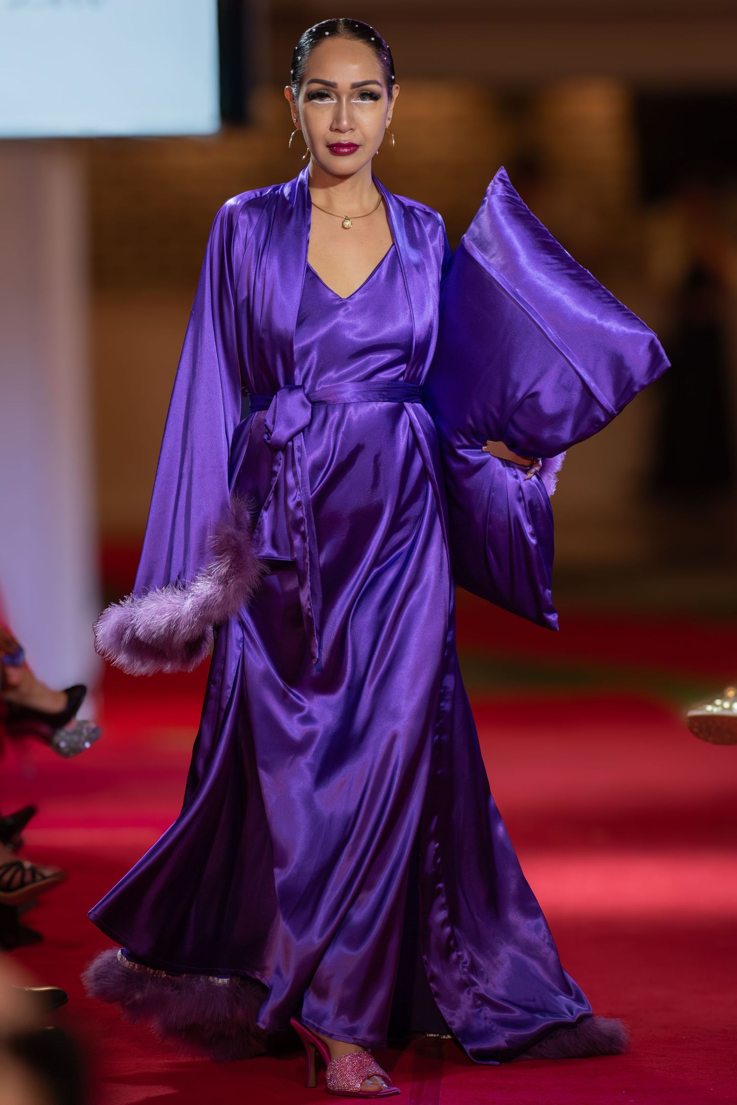 Model wearing a flowing evening gown under runway lighting.