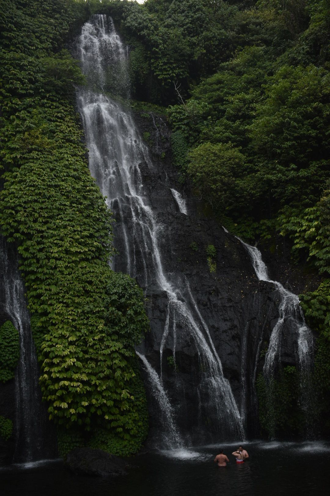 Candid picture of people swimming at the base of a waterfall.