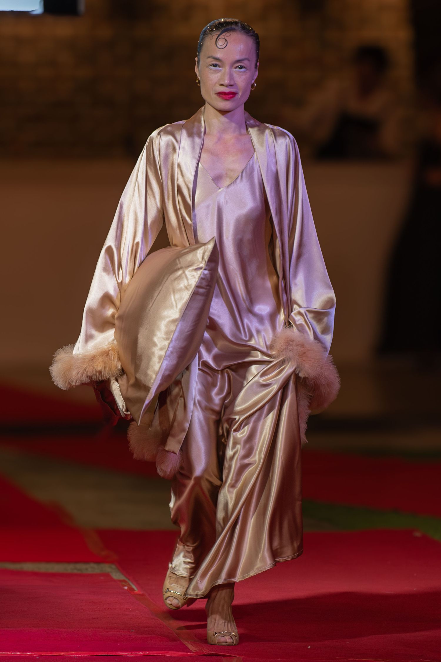 Model walking through dramatic lighting at an evening runway show in Brisbane.