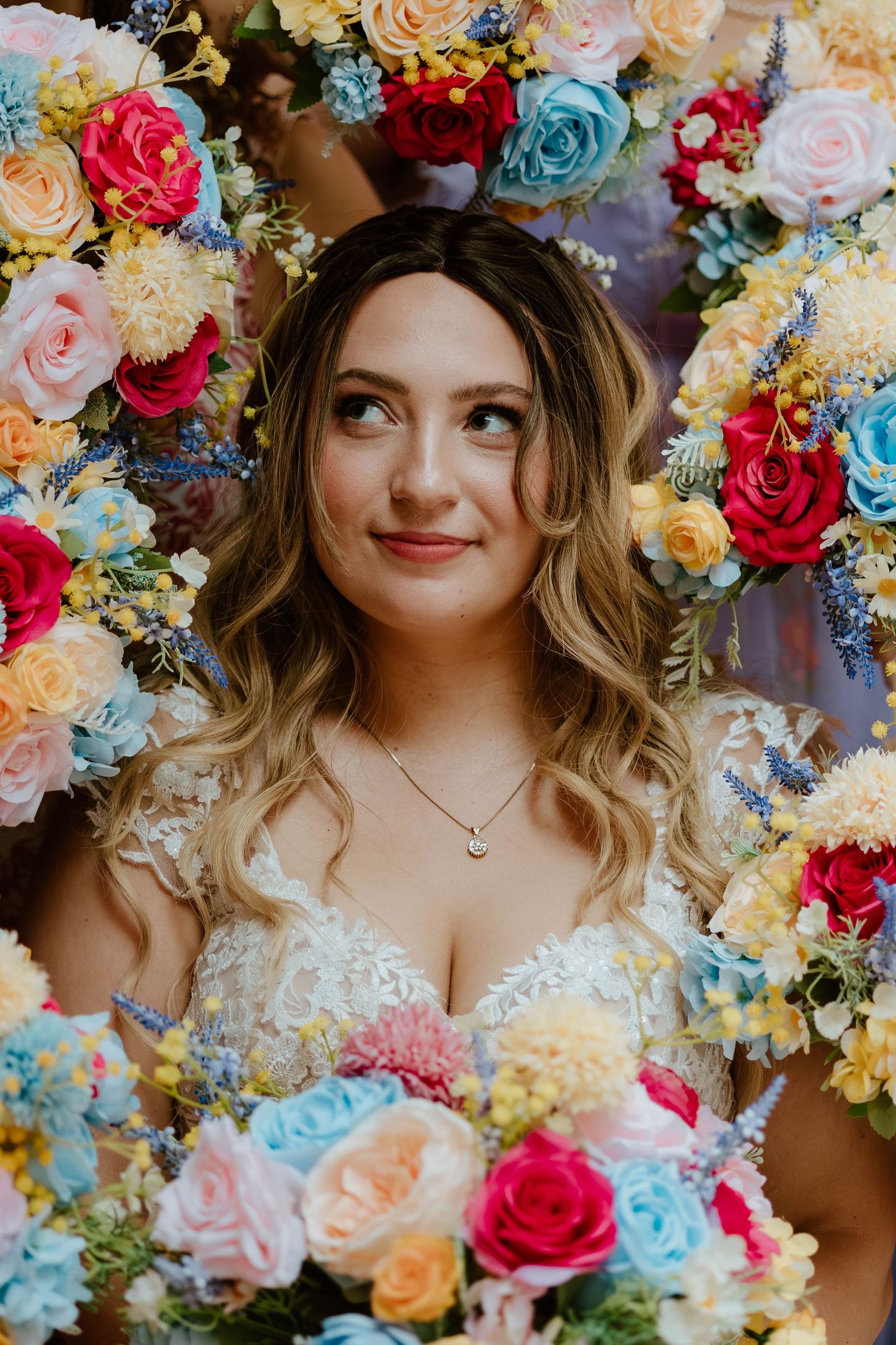 Bride holding a colorful bouquet with a floral backdrop behind her