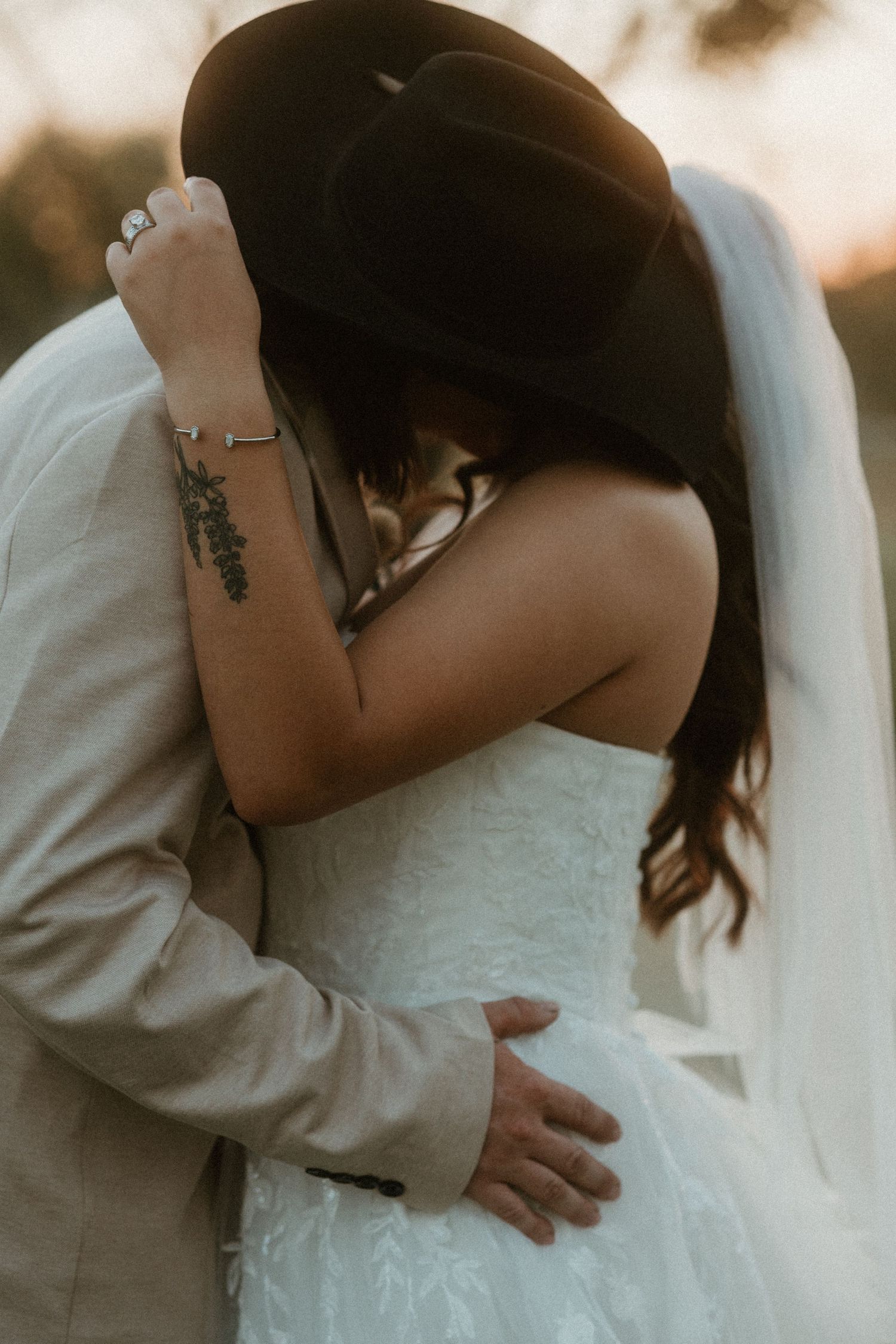 Bride and groom kissing behind cowboy hat. Wedding ring and dress.