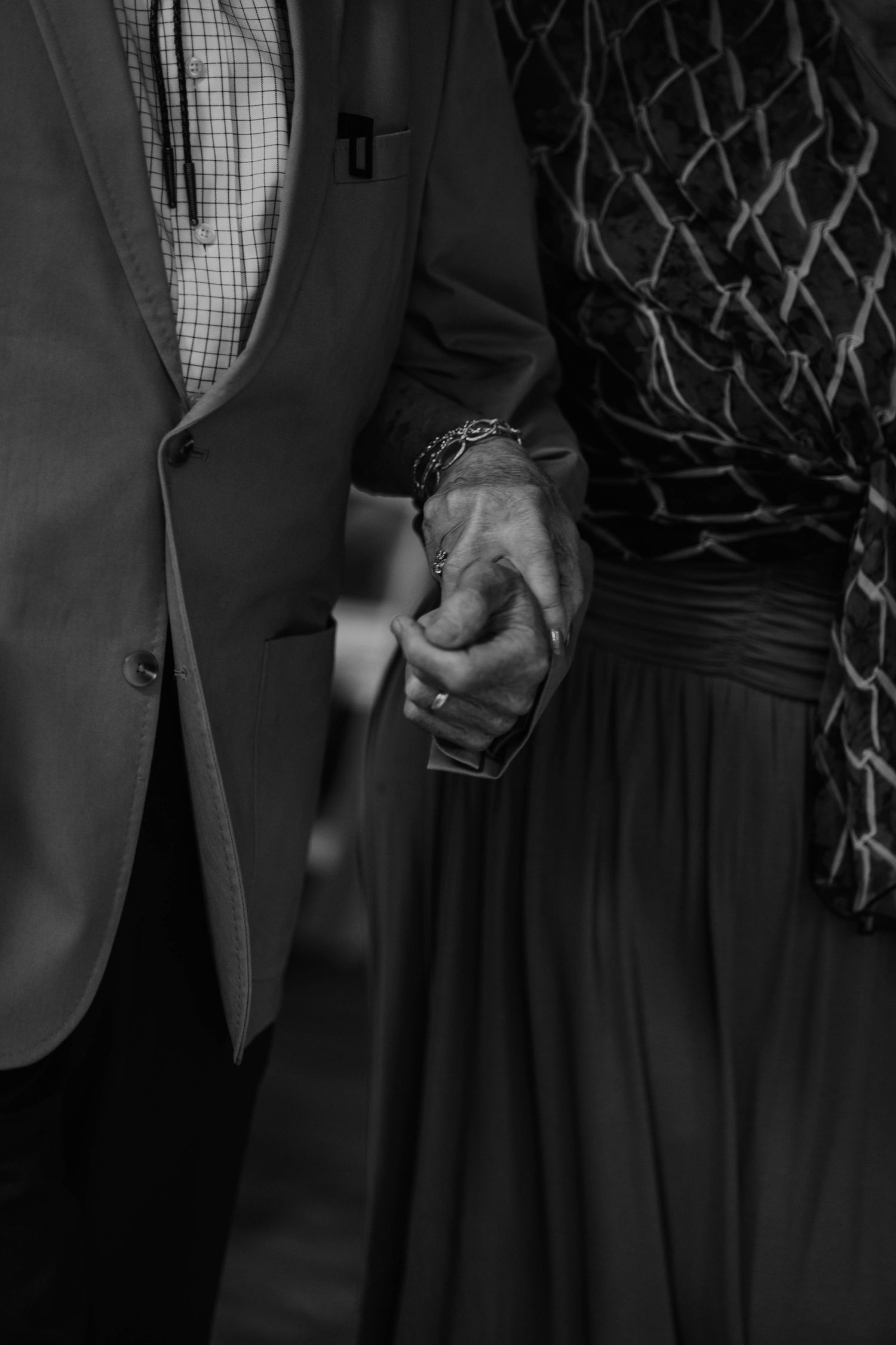 Black and white photo of grandparents holding hands walking down isle to their seats
