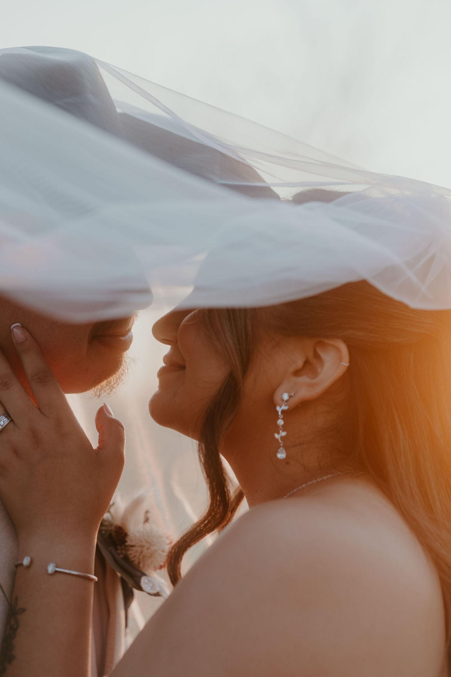 Bride and groom under wedding dress vail about to kiss.