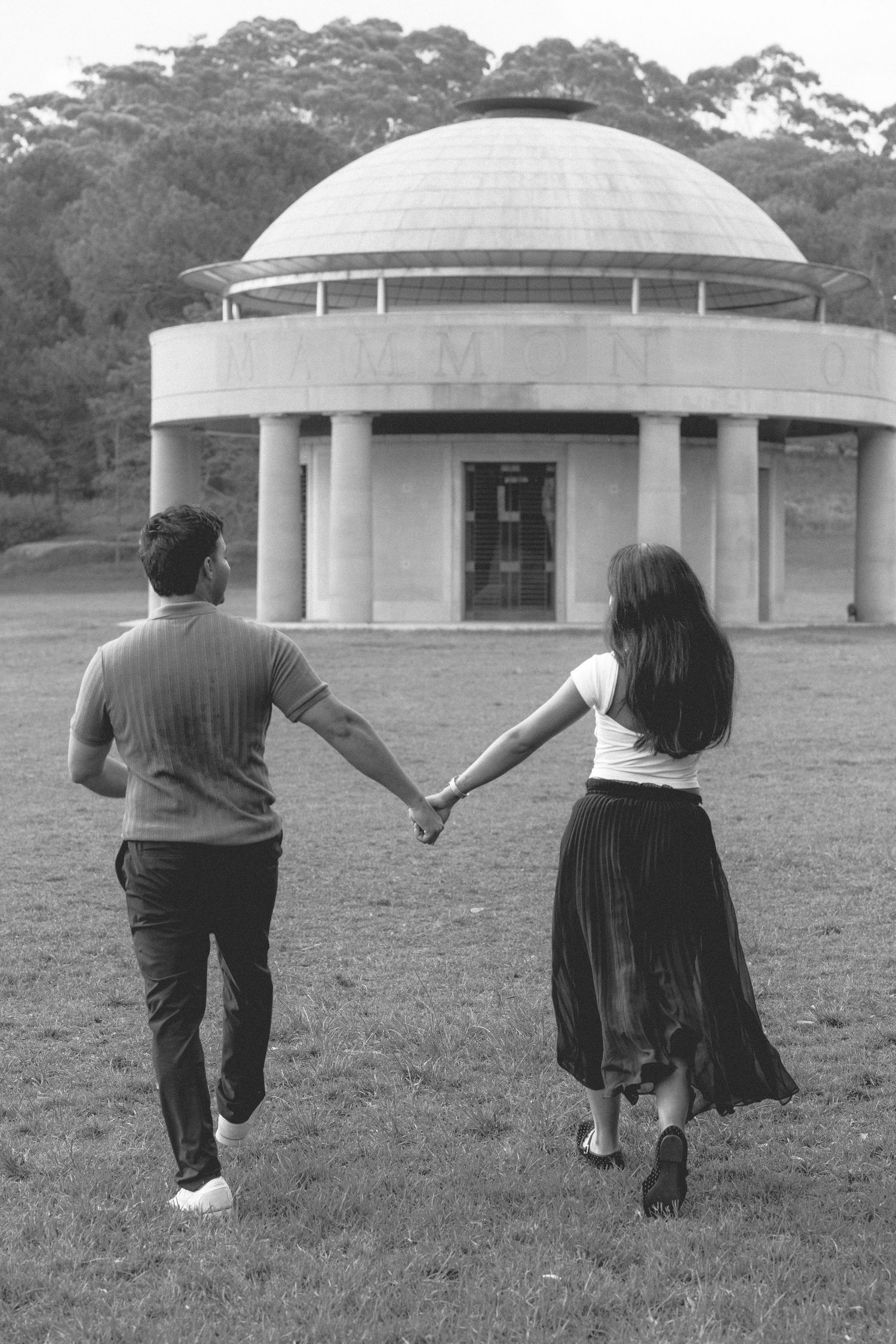 Couple holding hands walking toward a domed rotunda building in black and white.