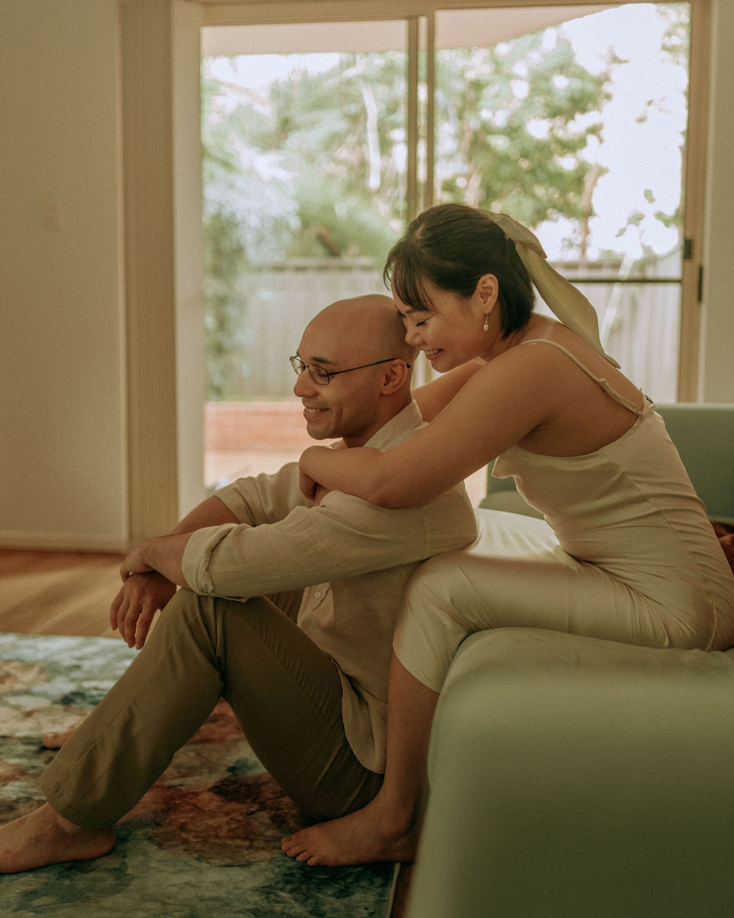 Couple sitting together on floor, woman resting head on mans shoulder indoors.