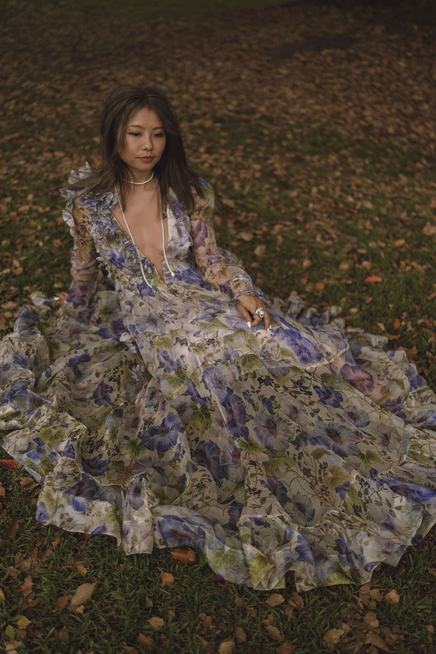 Woman in floral blue dress sitting on autumn leaves in a garden.