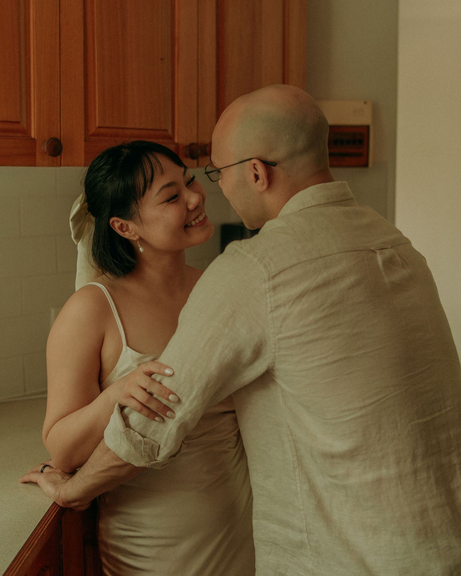Couple sharing a joyful smile and embrace in a warm kitchen, woman in satin dress looking happy.