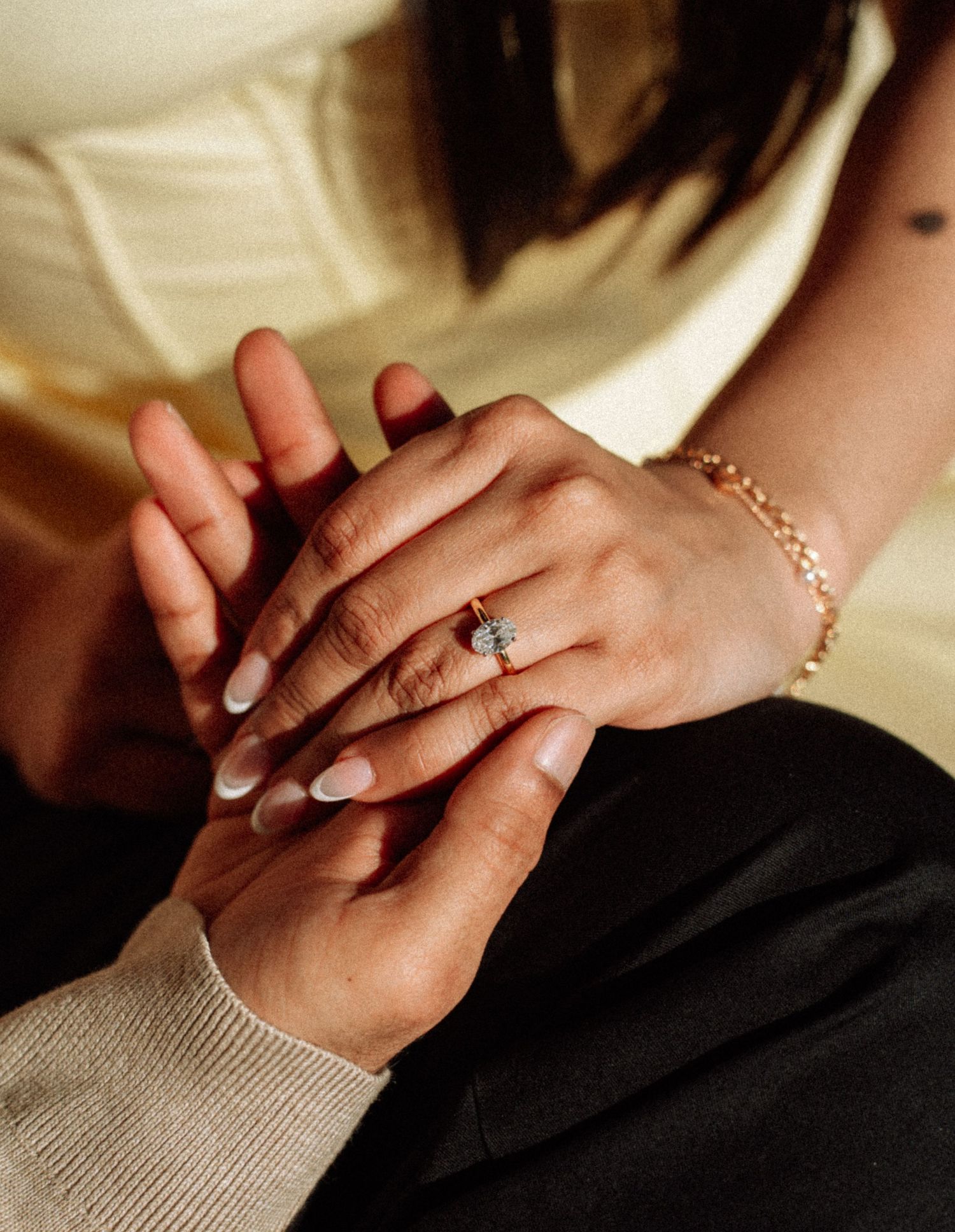 Close-up of hands with a diamond engagement ring on finger and gold bracelet, romantic proposal moment.