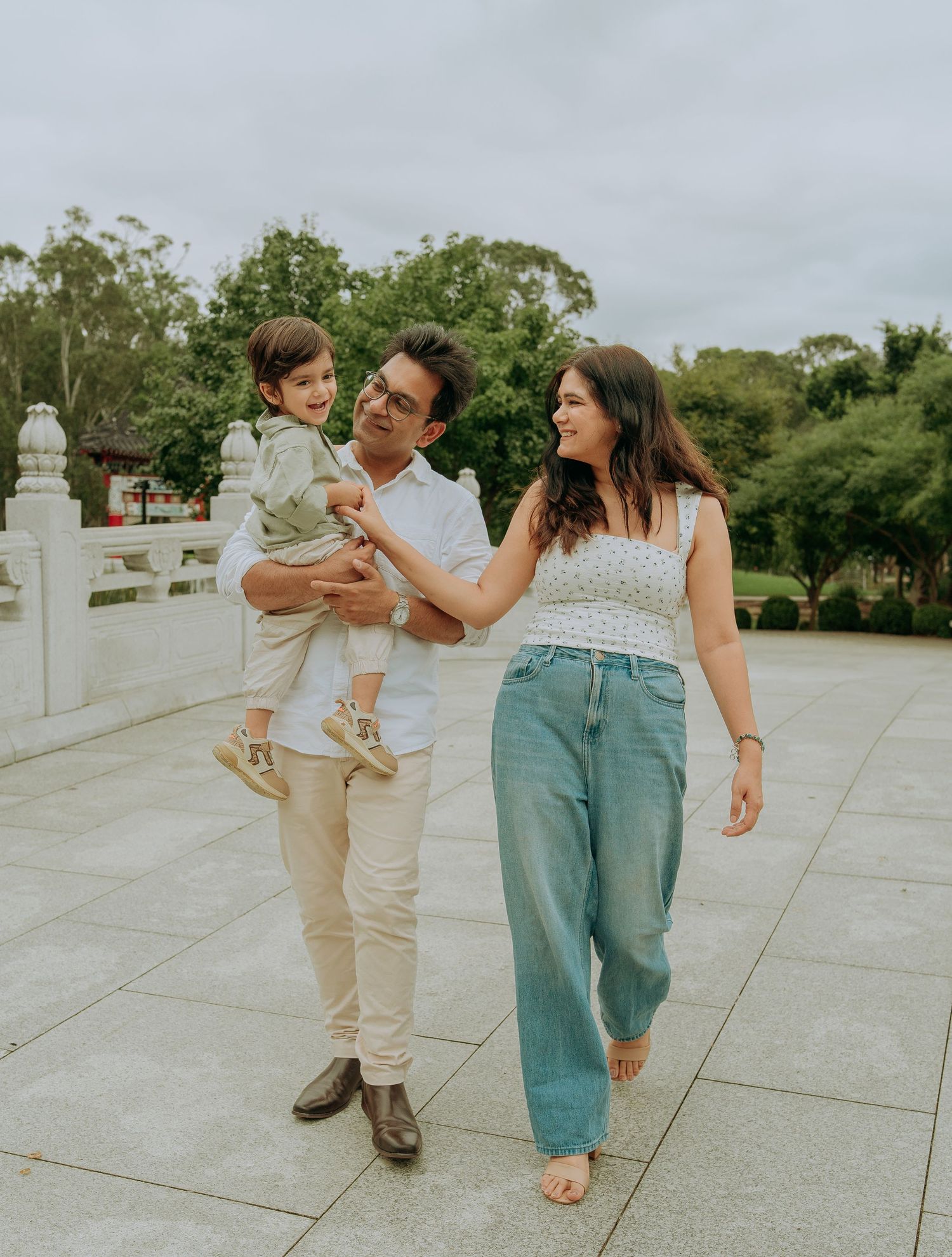Happy family of three strolling outdoors, father holding toddler son while mother smiles at child.
