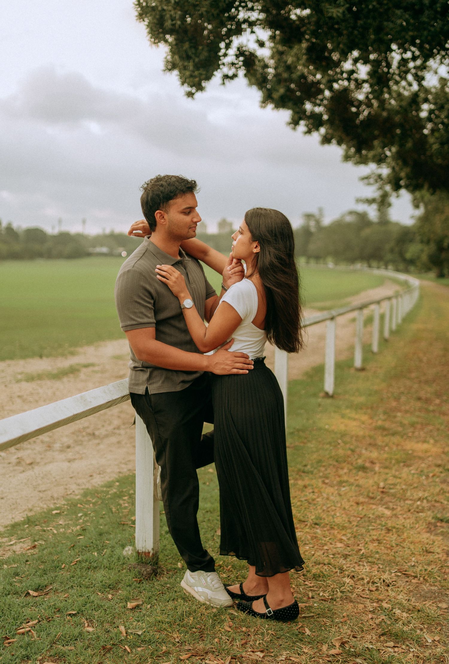 Romantic couple embracing near a white fence in a lush green park.