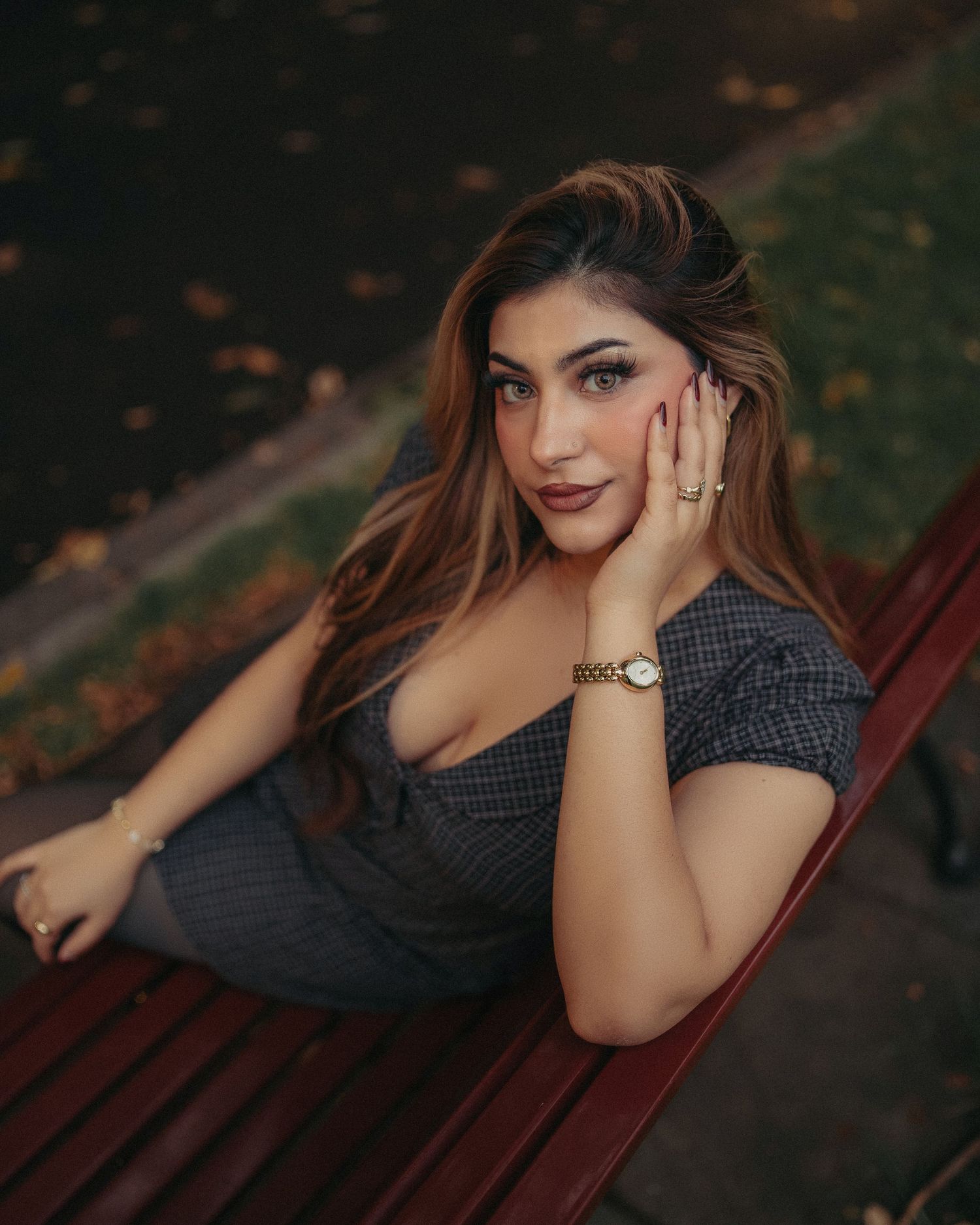 Attractive woman in plaid dress sitting on a red bench in an autumn park.
