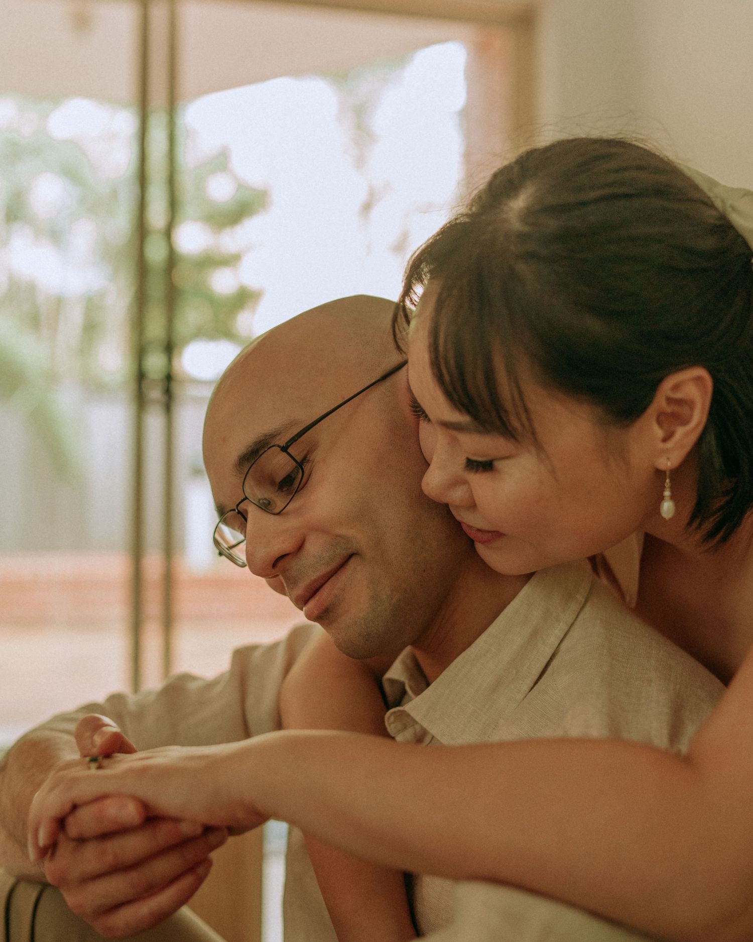 Close-up of loving couple embracing, bald man with glasses smiling as woman rests her head on his shoulder.