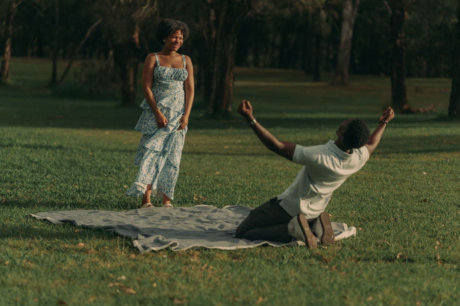 A joyful couple spreads a picnic blanket on lush green grass in a sunlit park during golden hour.