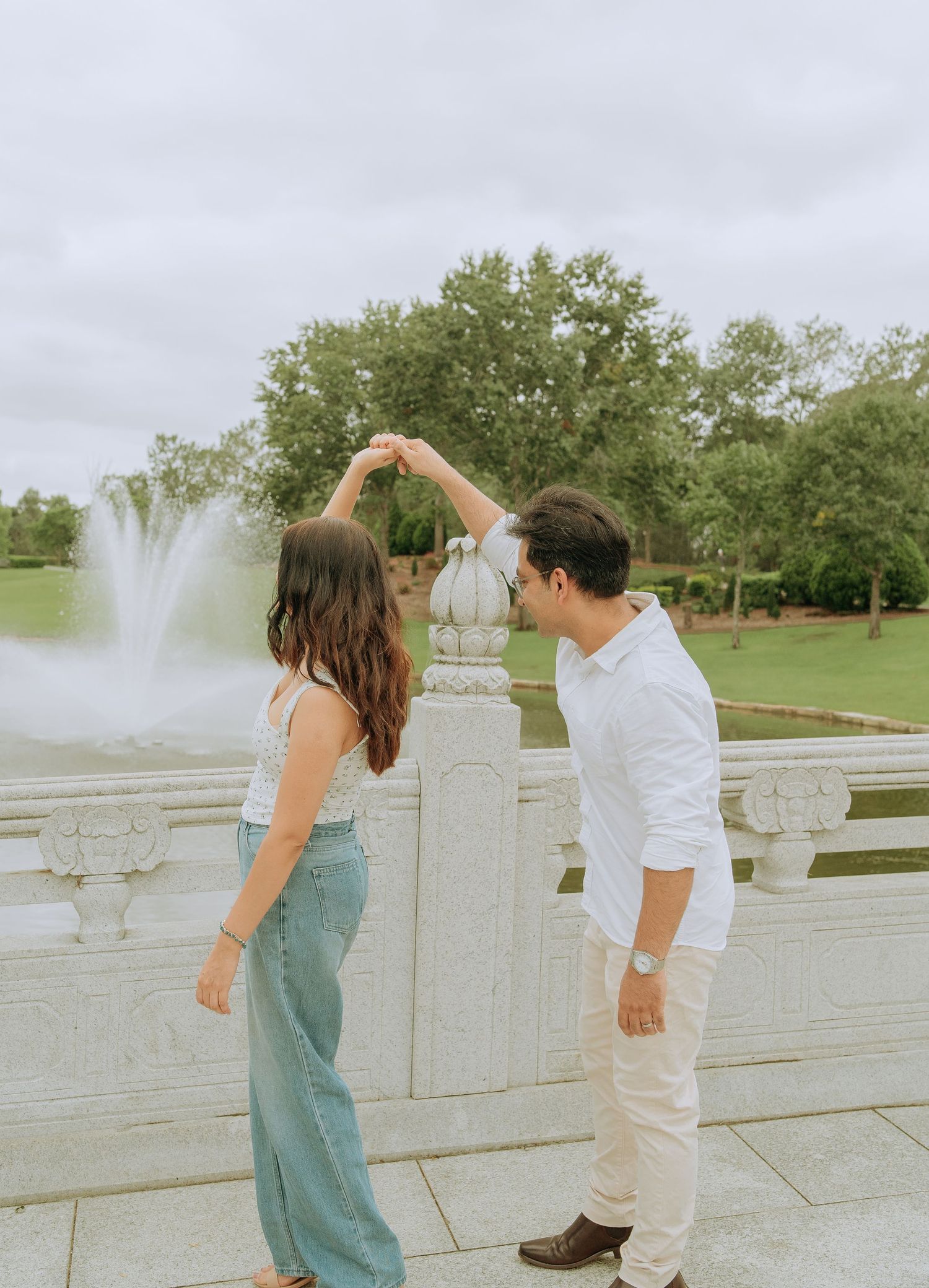 A couple dances together on a marble terrace near a fountain, man spinning woman in a joyful moment.
