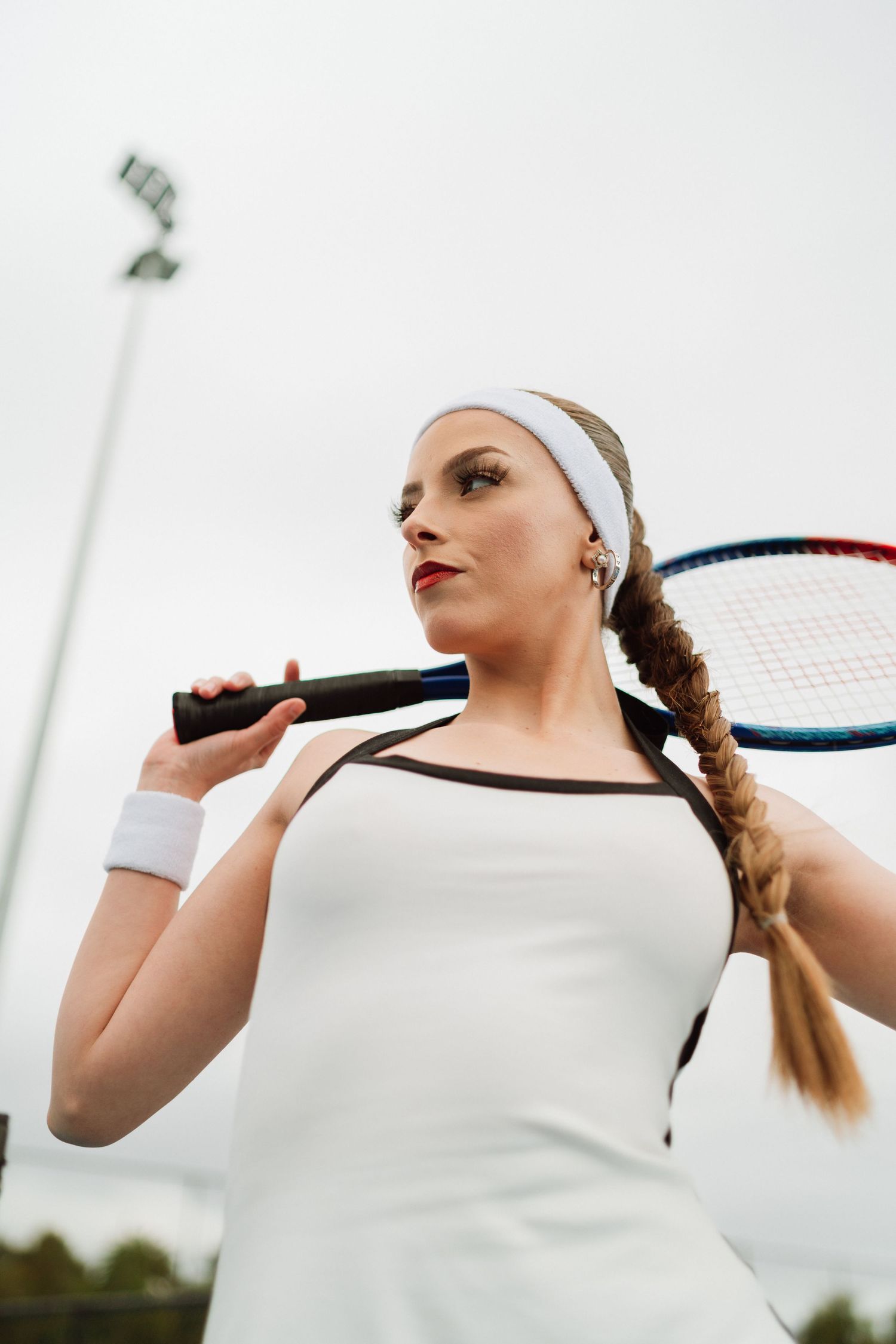 Close-up of female tennis player in white outfit holding racket over shoulder outdoors.